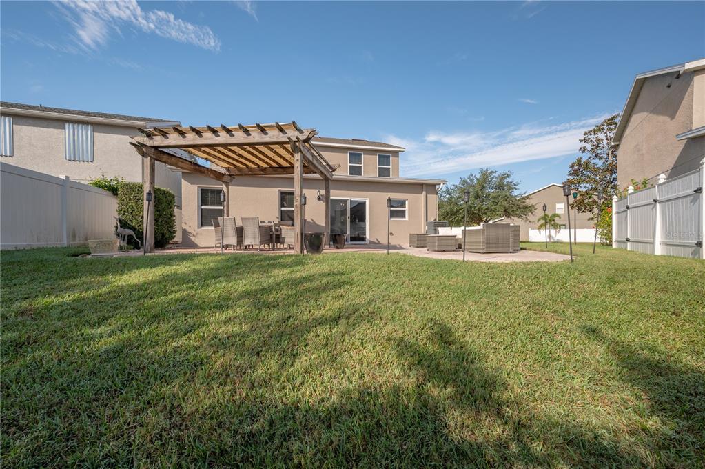 Two-story home with a grassy backyard, wooden pergola, and patio seating.