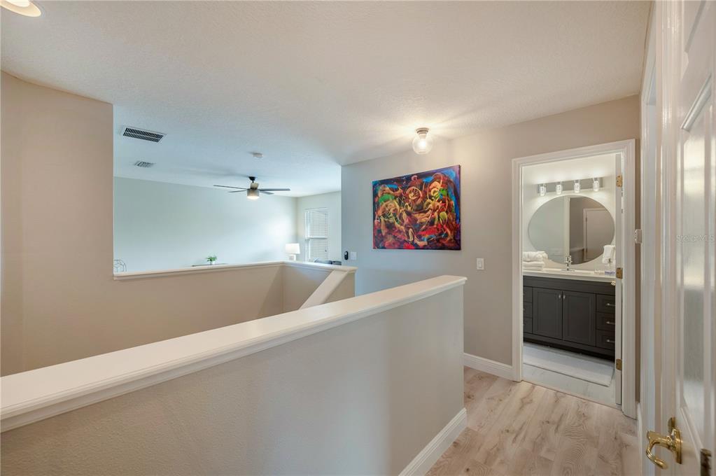 Upstairs landing with white stair railing and colorful wall art beside an open bathroom doorway.