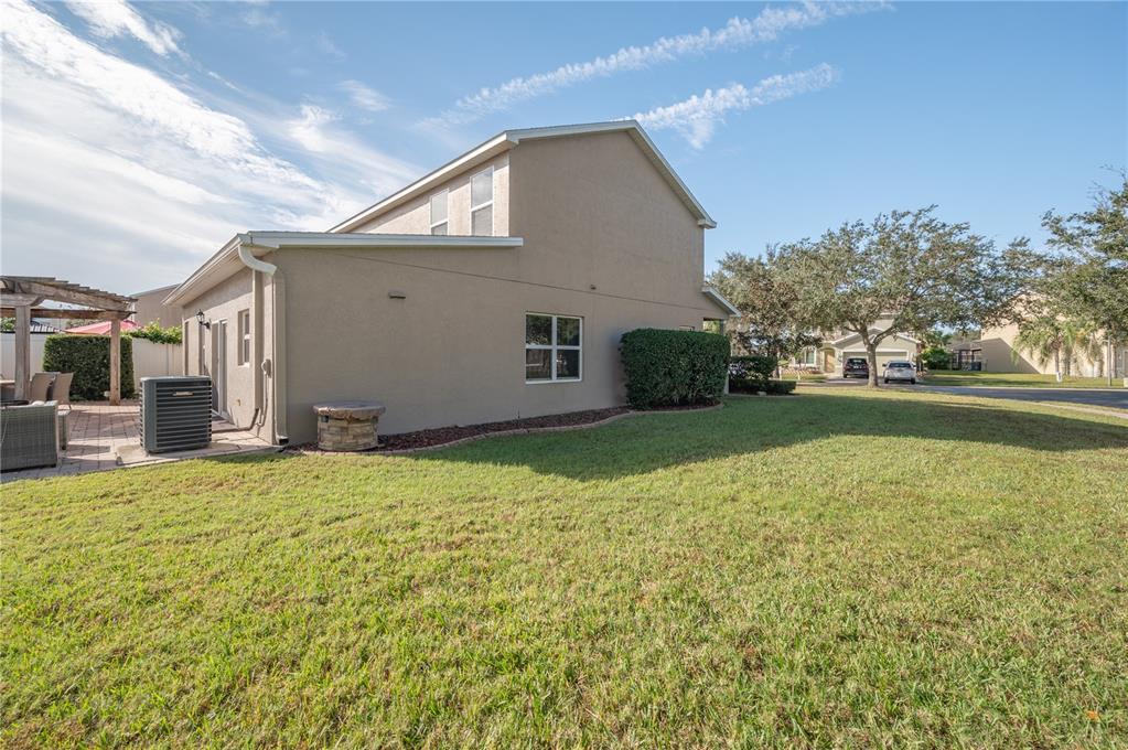 Two-story beige stucco home beside a broad lawn, viewed from the side and rear.