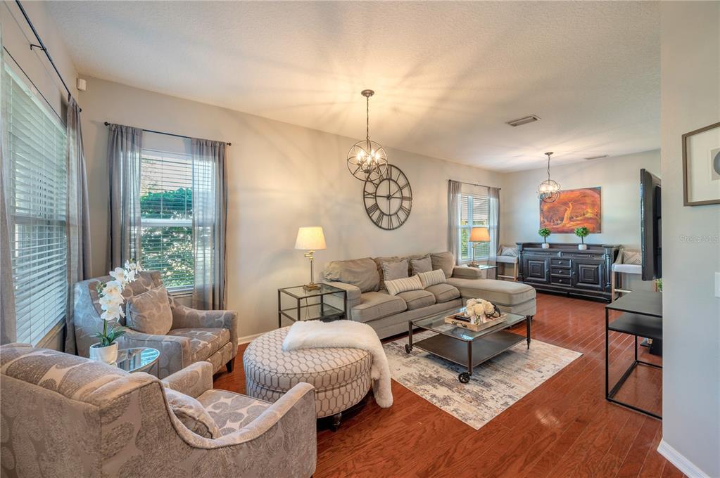Furnished living room with a gray sectional, patterned armchairs, hardwood floors, and large windows.