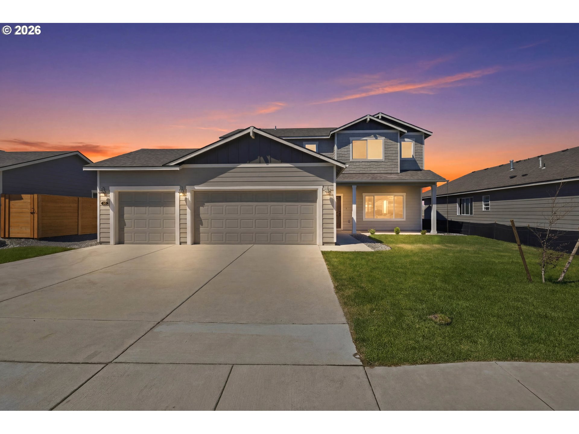Two-story gray house with a two-car garage and broad driveway at dusk.