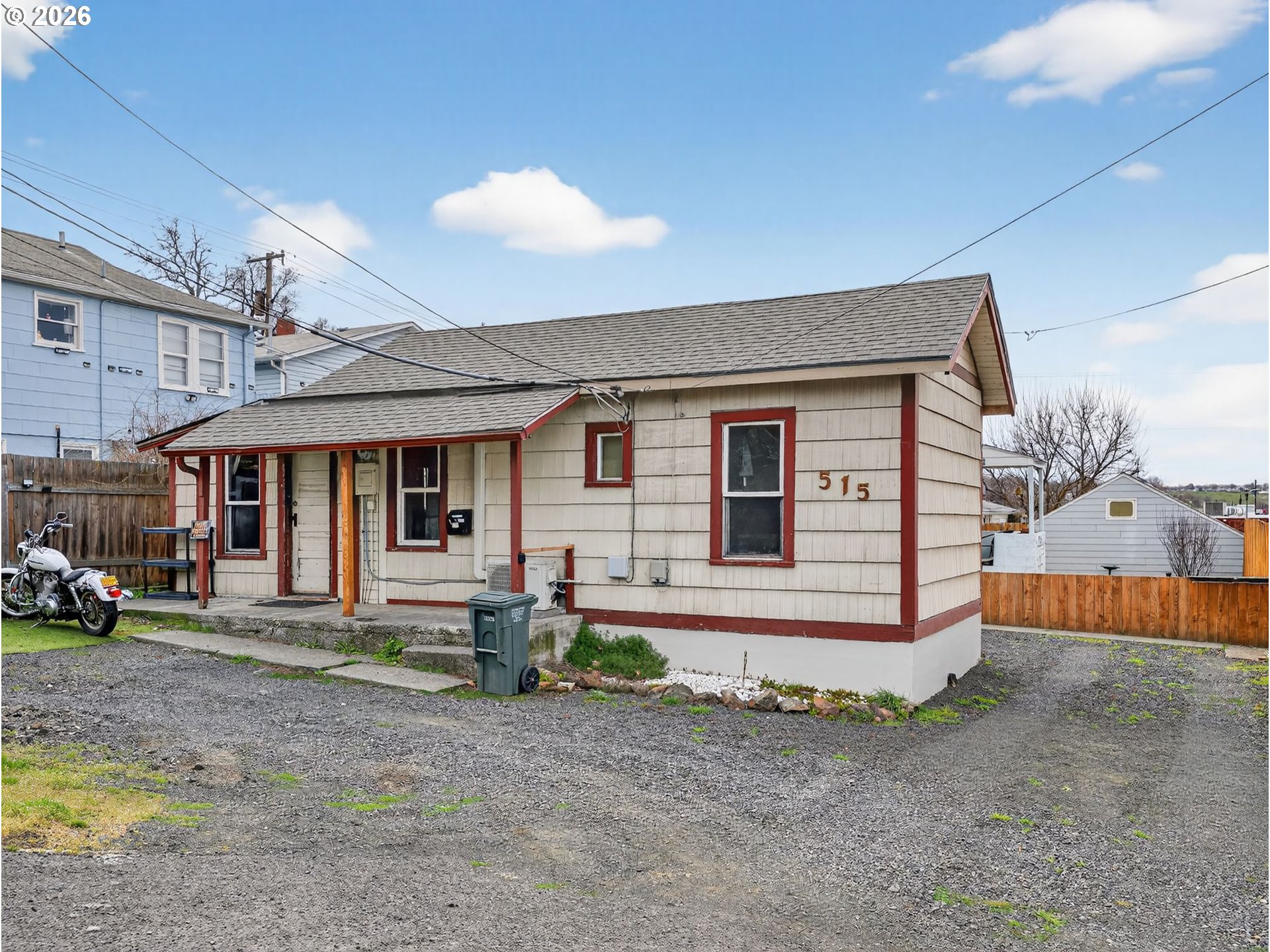 Single-story beige house with red trim, address 515, and a gravel yard with a motorcycle.