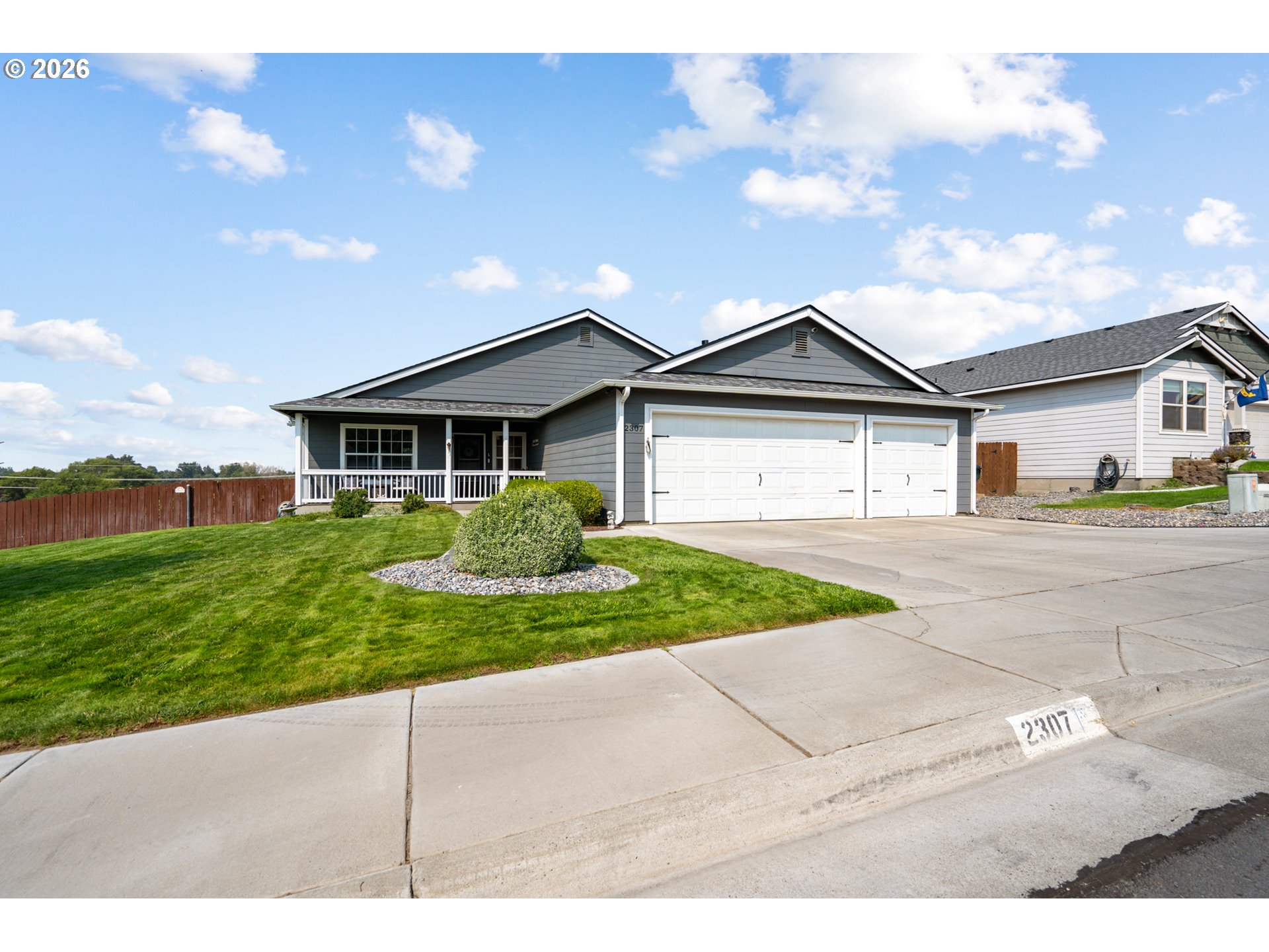 Gray single-story home with a covered porch, double garage, landscaped lawn, and wide concrete driveway.