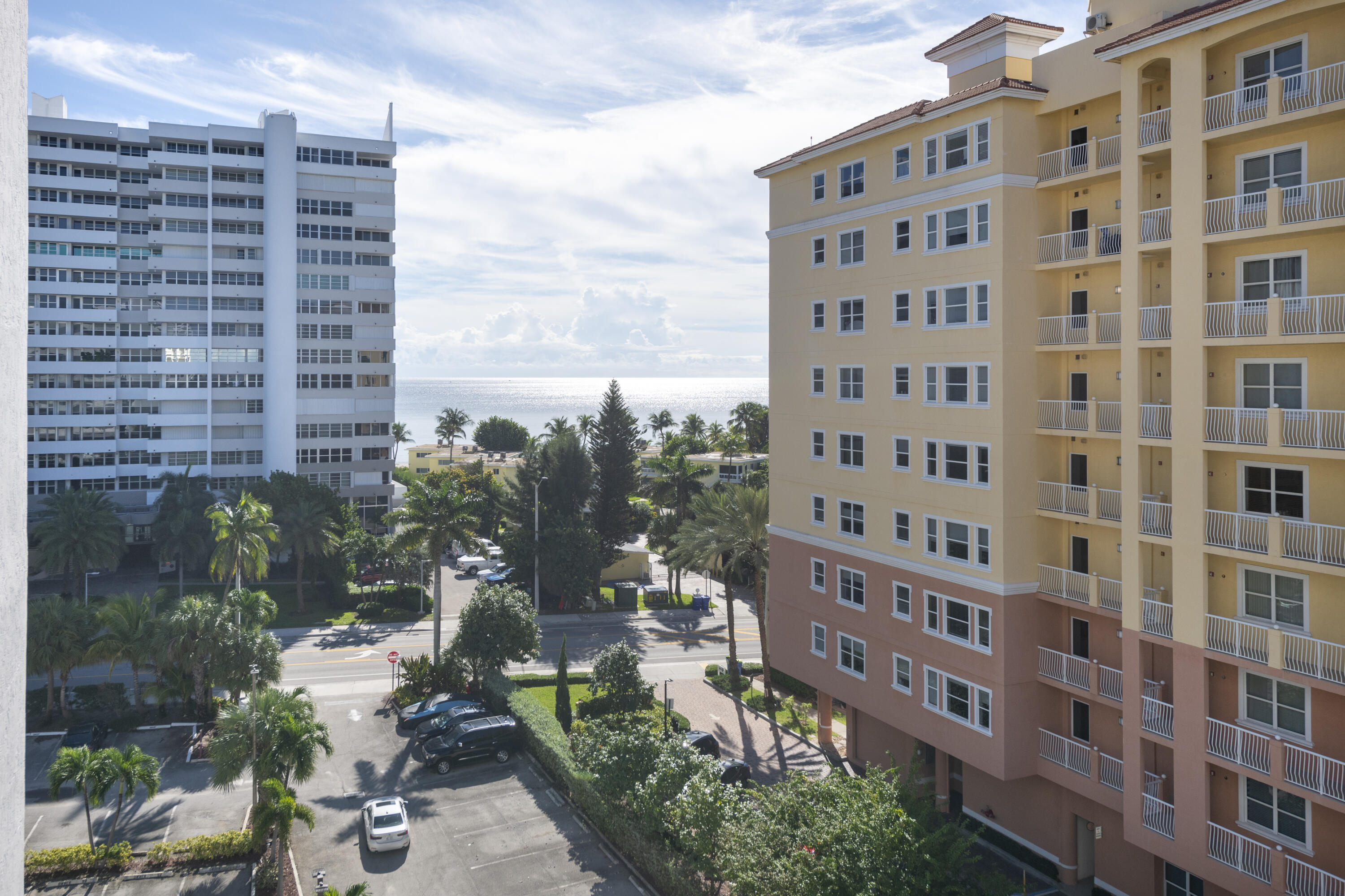 Ocean view between condominium buildings, with palm trees and a parking area below.
