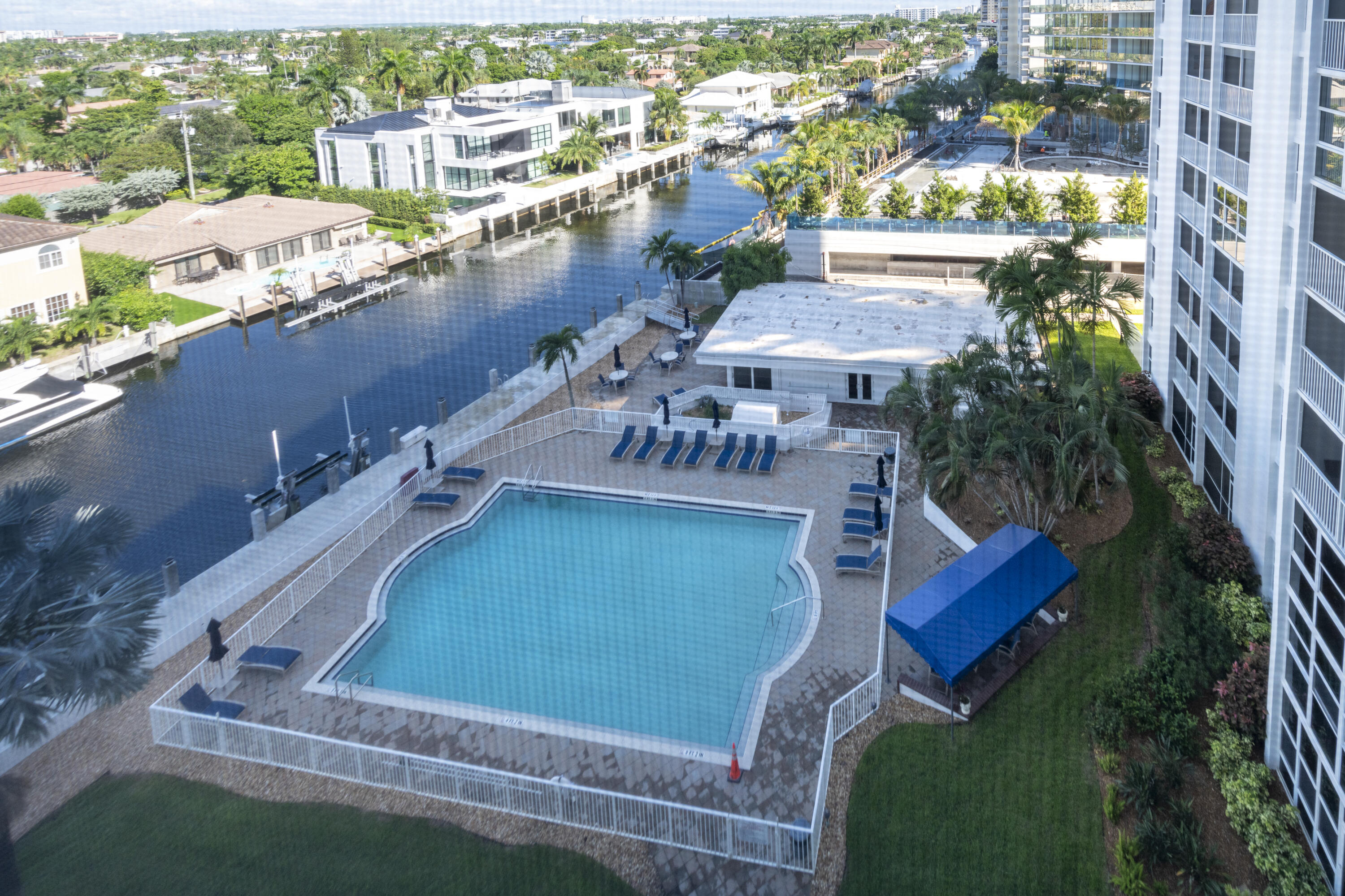 Condominium pool deck beside a canal, with lounge chairs, palms, and waterfront homes.