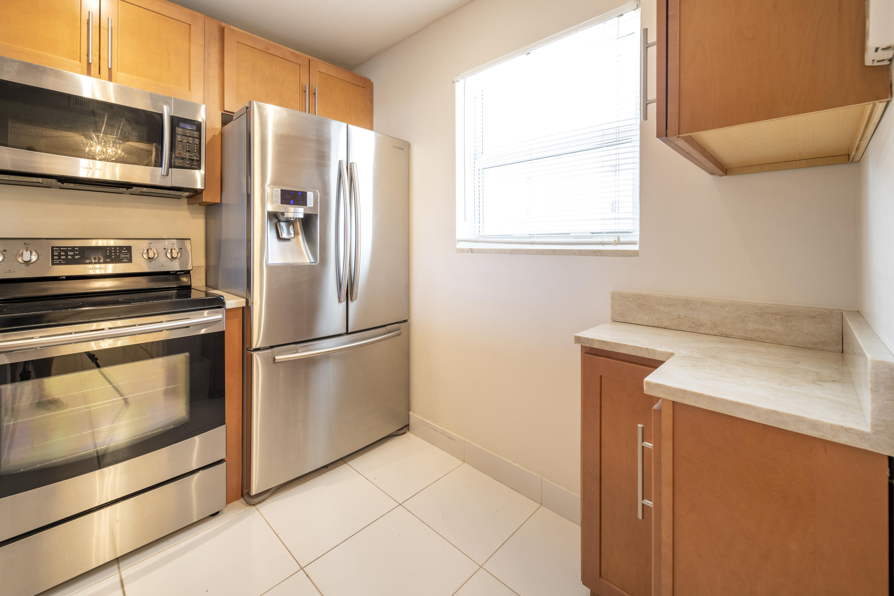 Kitchen with wood cabinetry, stone counters, and stainless steel refrigerator, microwave, and range.