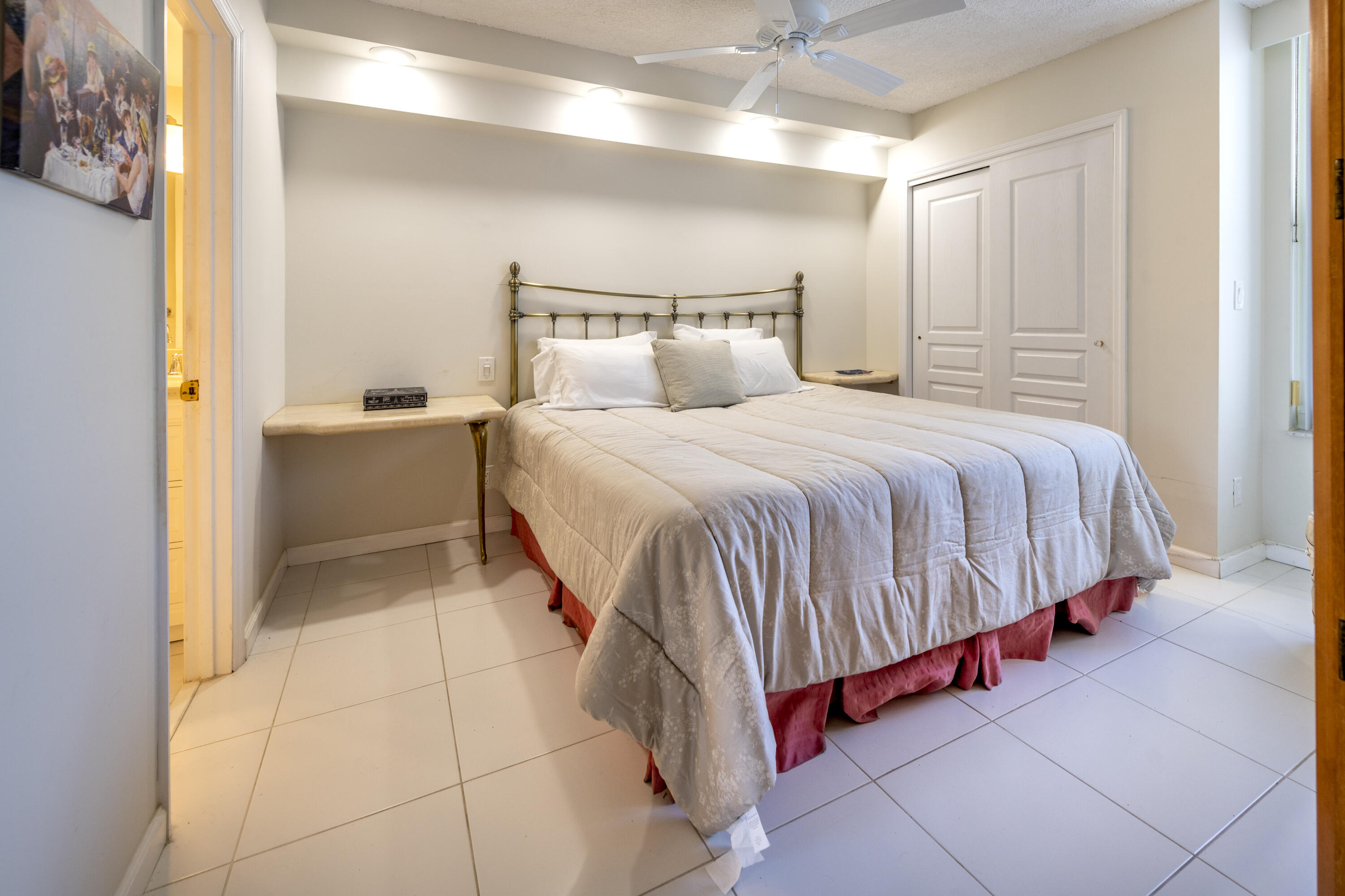 Furnished bedroom with a brass headboard, white bedding, tiled floor, and ceiling fan.