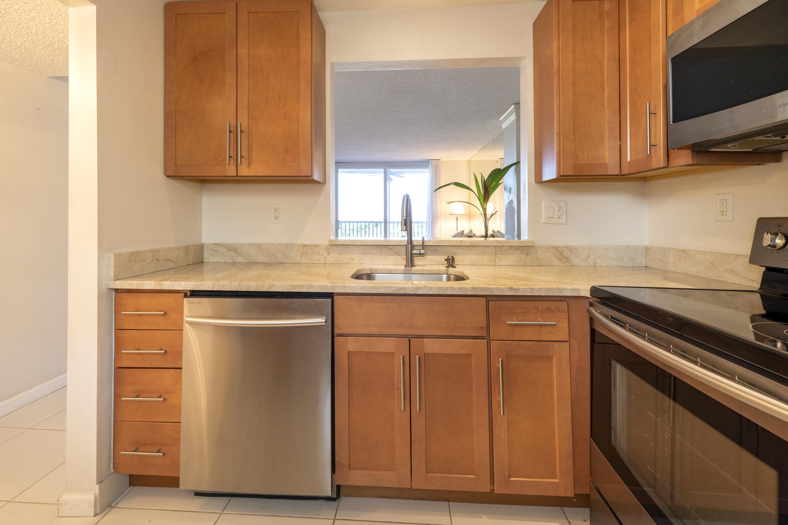 Kitchen with warm wood cabinets, stone counters, stainless dishwasher, and a pass-through to the living area.