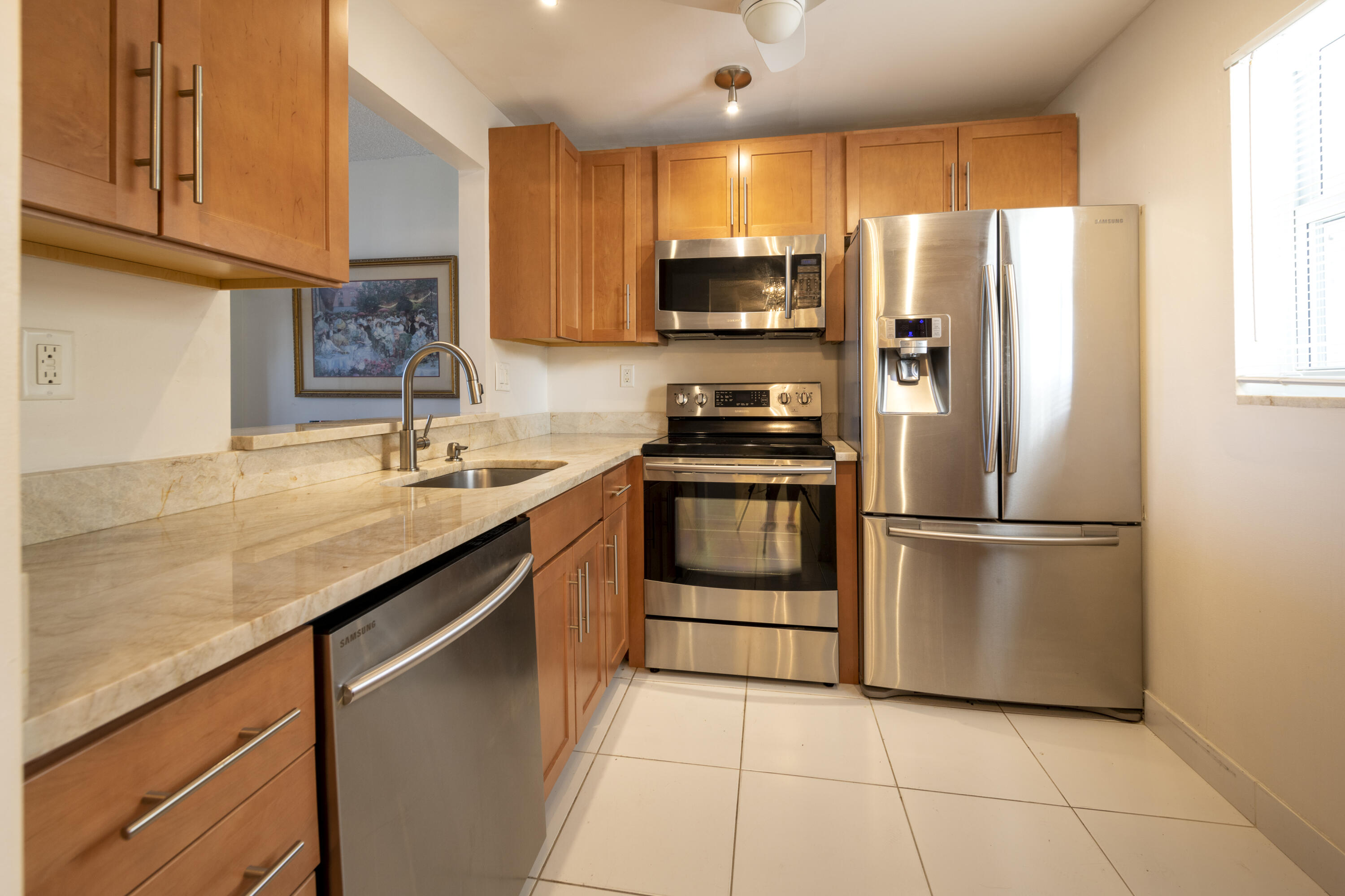 Condominium kitchen with wood cabinets, pale stone counters, and stainless-steel appliances.