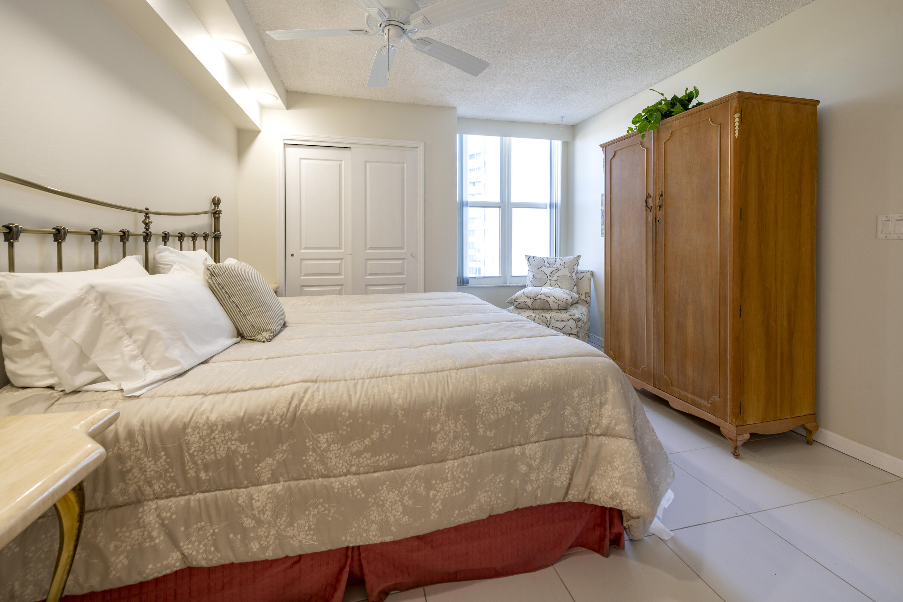 Bedroom with a large bed, brass headboard, and wooden armoire beside bright windows.