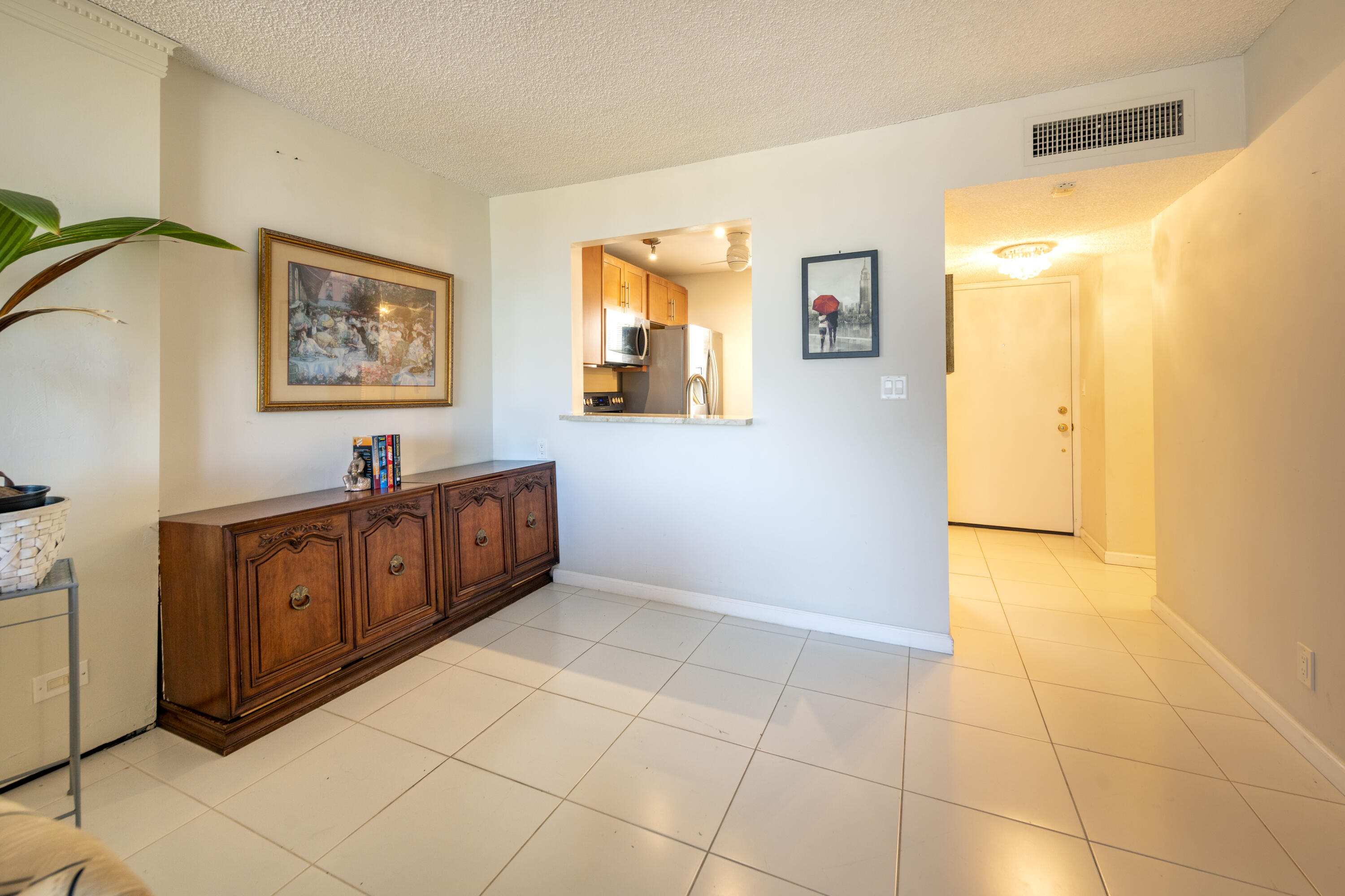 Condo entry with a wooden sideboard, tiled floor, kitchen pass-through, and brightly lit hallway.