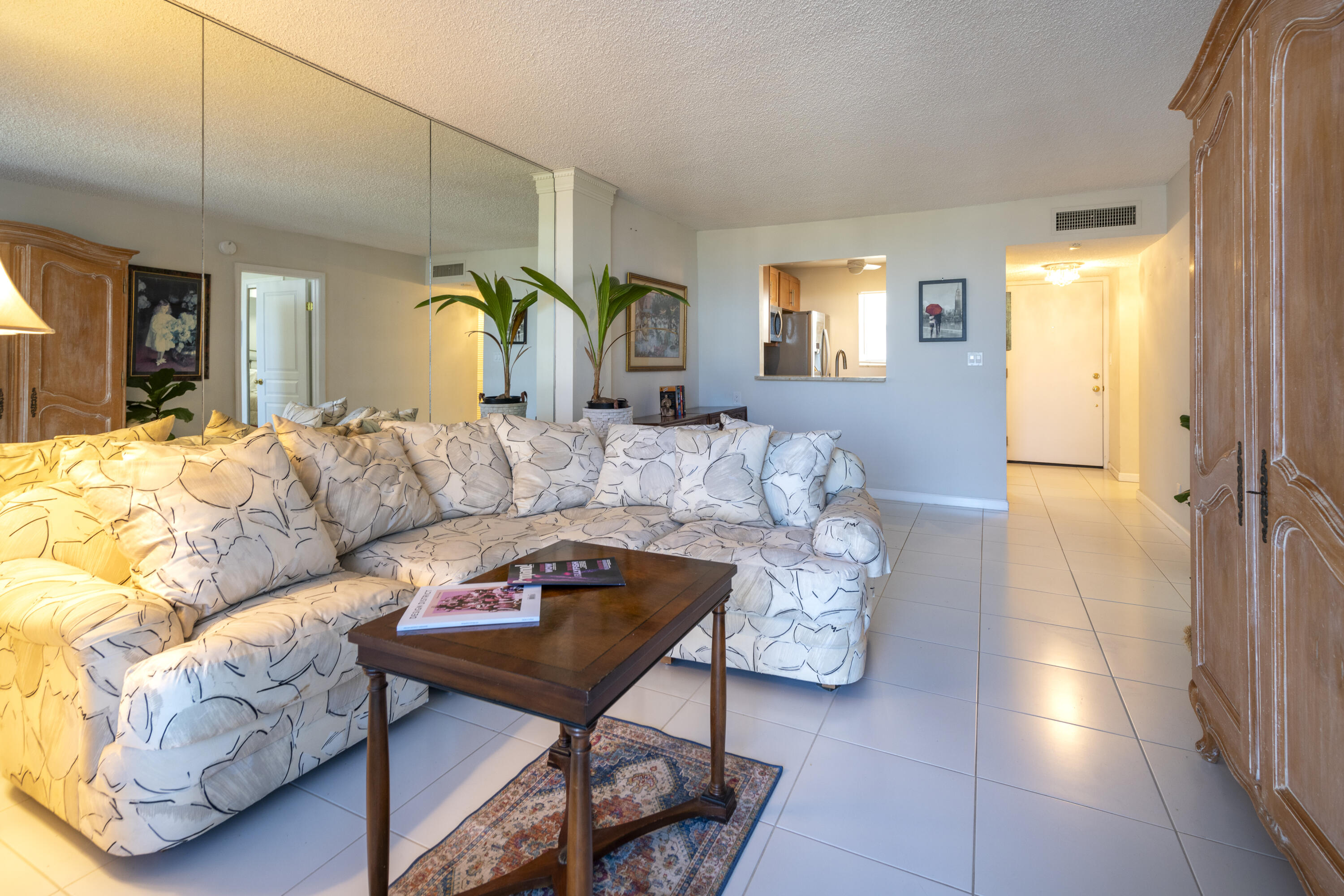 Living room with a large patterned sectional, mirrored wall, and pass-through to the kitchen.
