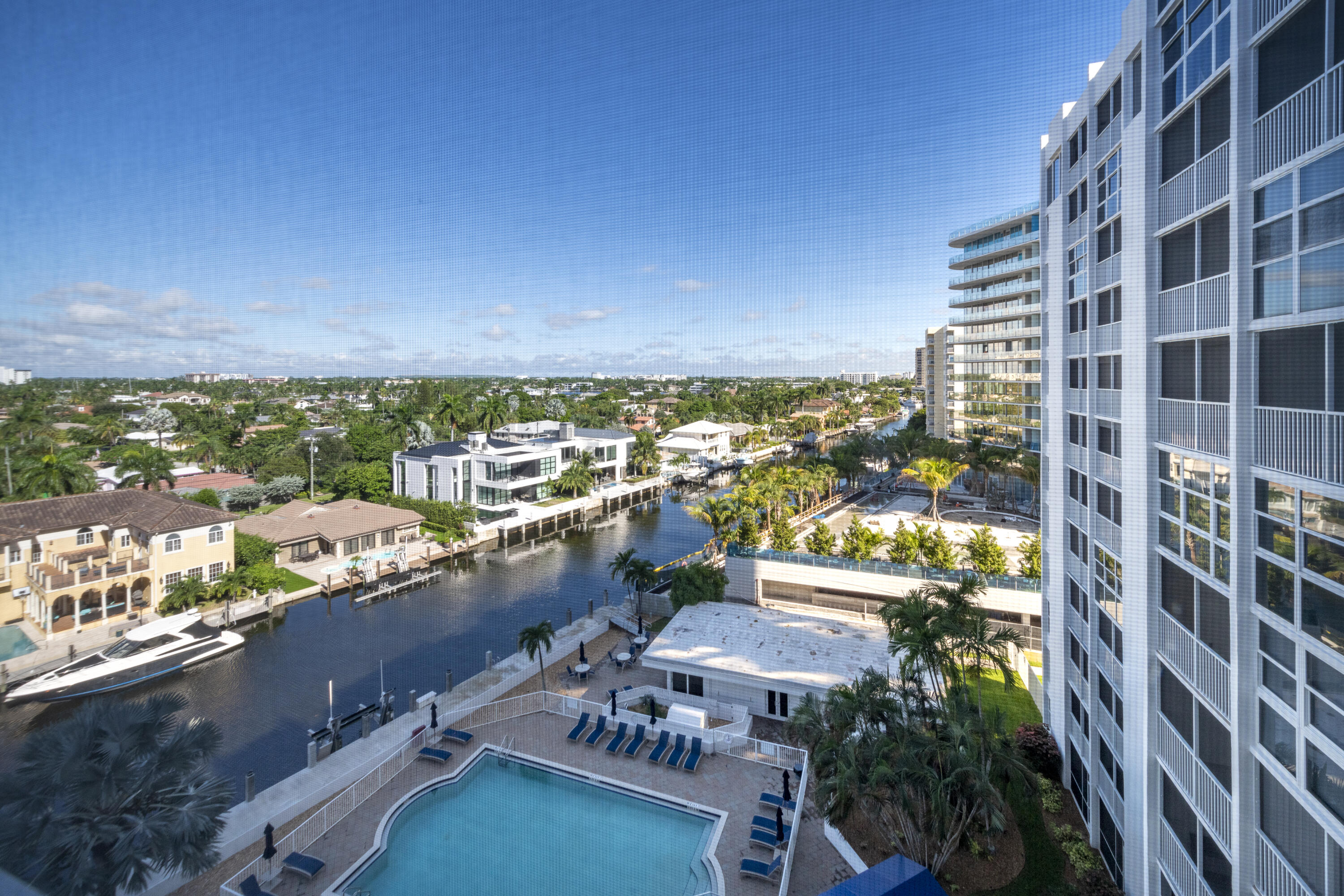 High-rise condo pool deck overlooking a canal, docked boat, and waterfront homes.