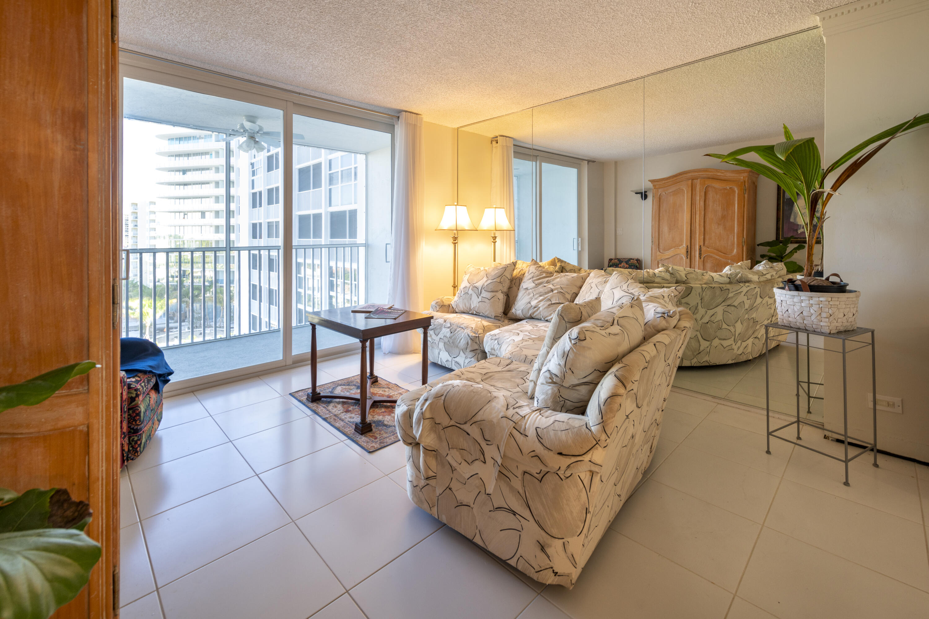 Furnished condo living room with patterned sofas and sliding doors overlooking neighboring high-rises.