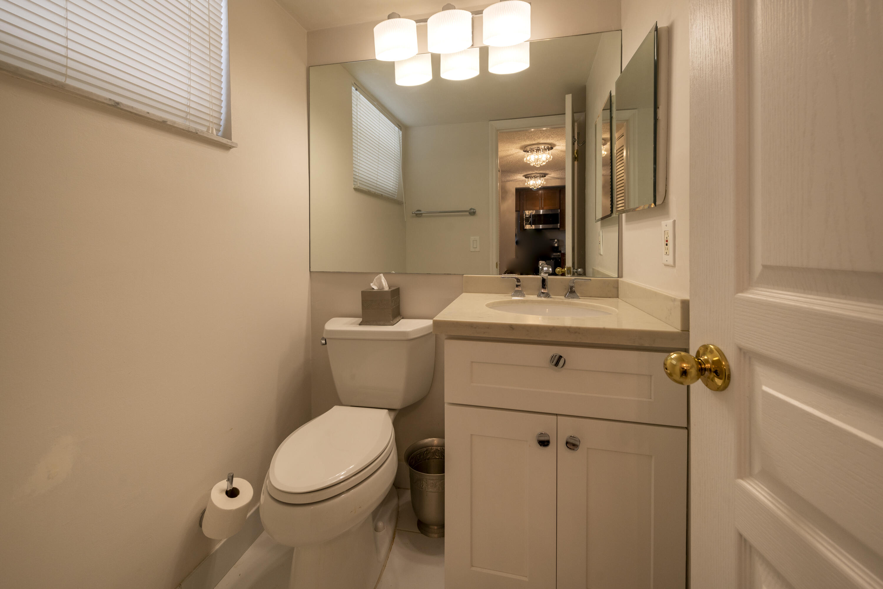 Bathroom with a cream vanity, large mirror, and toilet beside a window with blinds.