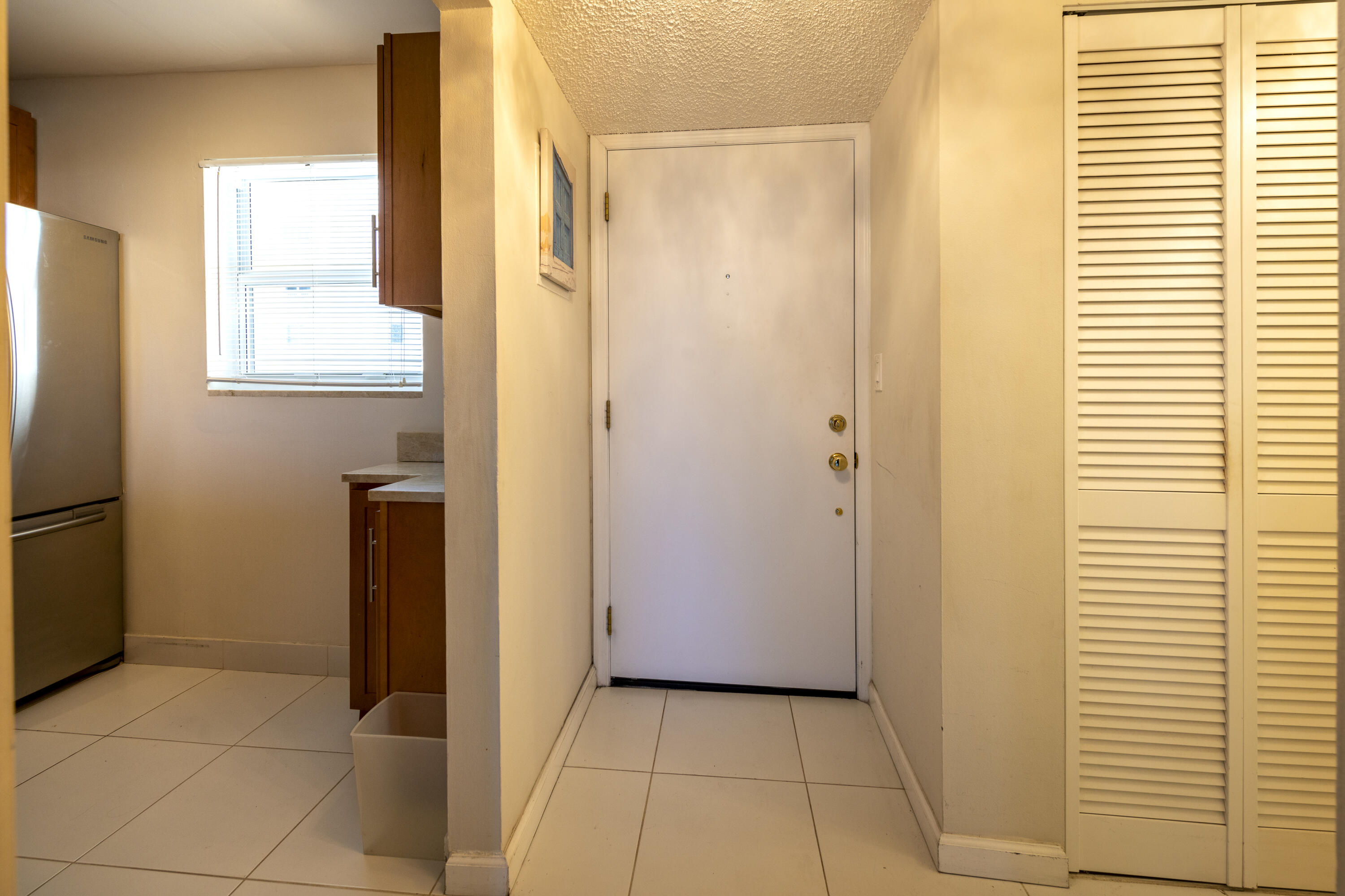 Entry hall with tiled floors, louvered closet doors, and a kitchen visible beyond.