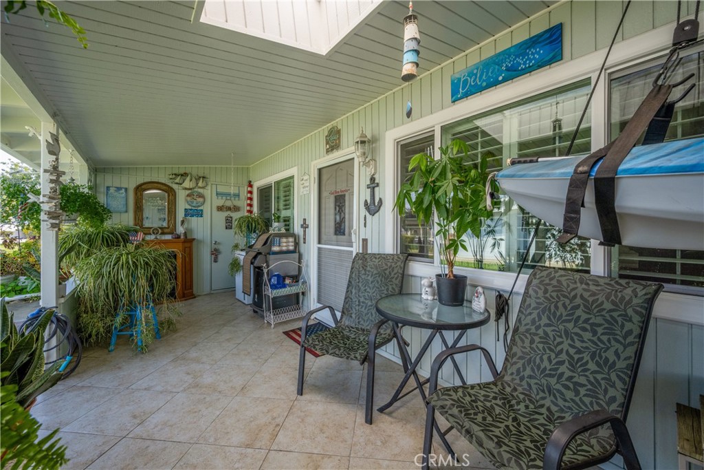 Covered patio with patterned chairs, potted plants, tiled floor, and a kayak suspended overhead.