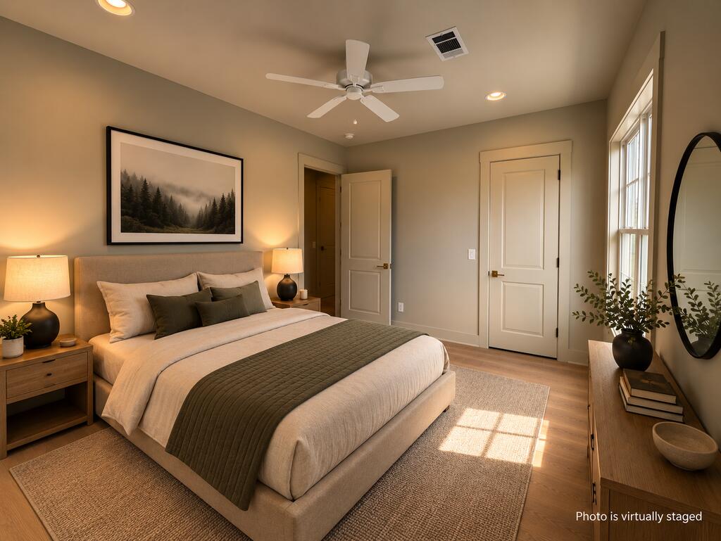 Virtually staged bedroom with an upholstered bed, matching nightstands, ceiling fan, and sunlight through tall windows.