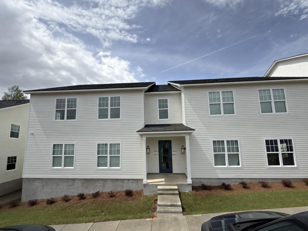 White two-story residential building with a recessed central entrance and a walkway across the front lawn.