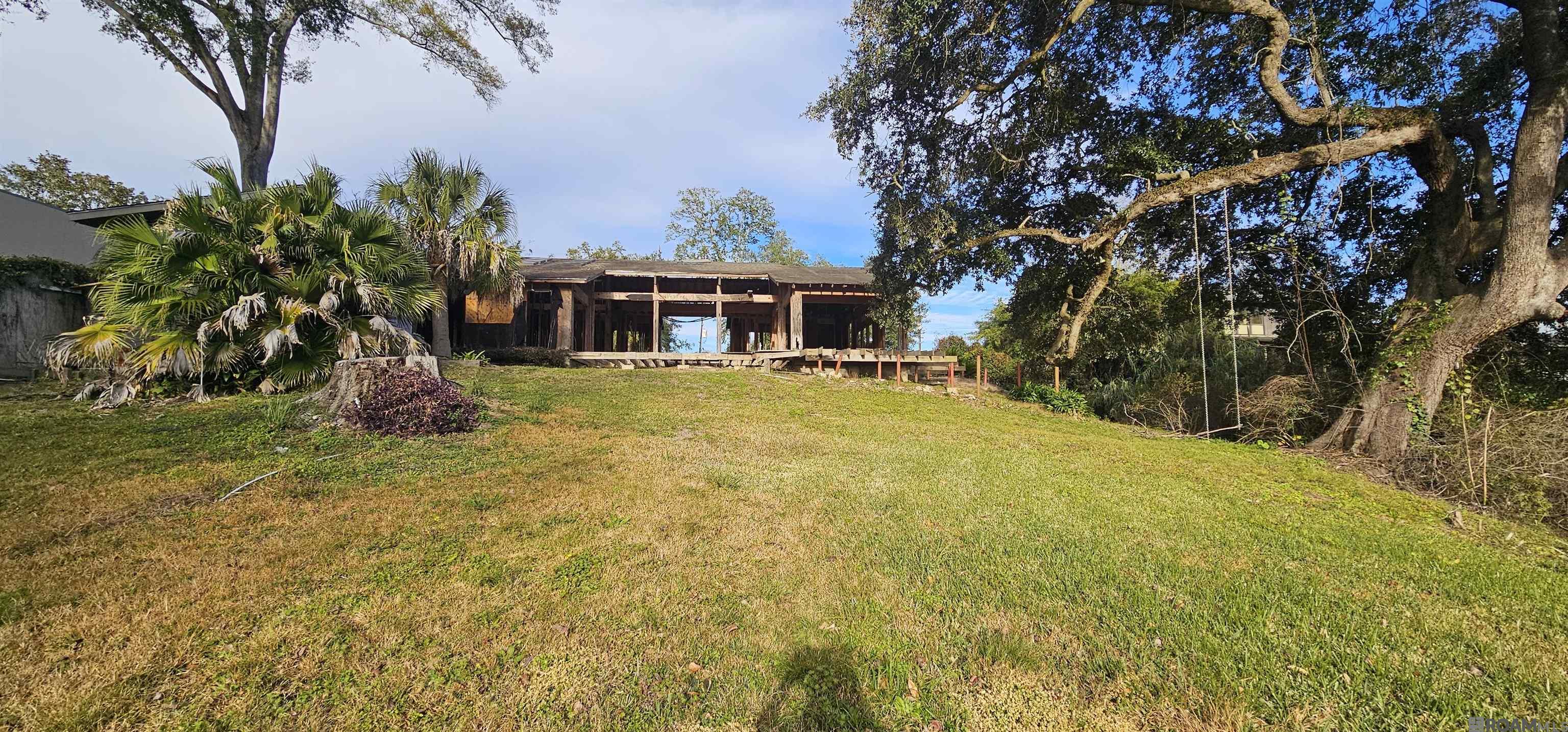 Single-story home with exposed porch framing behind a broad lawn and mature trees.