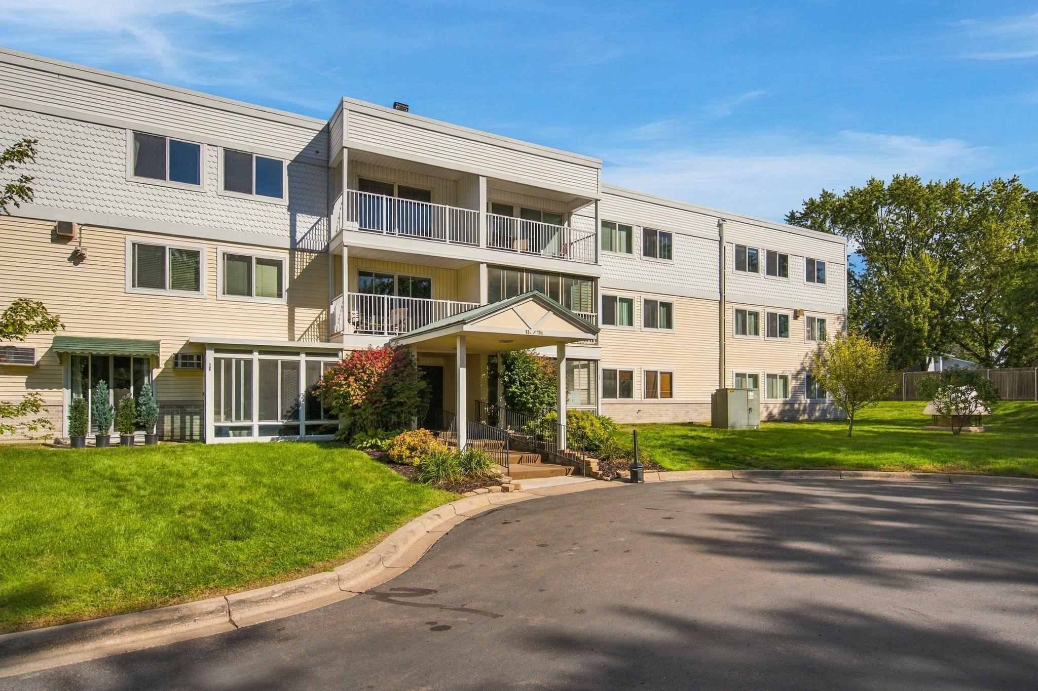 Multi-story condominium building with balconies, a covered entrance, and a landscaped lawn.
