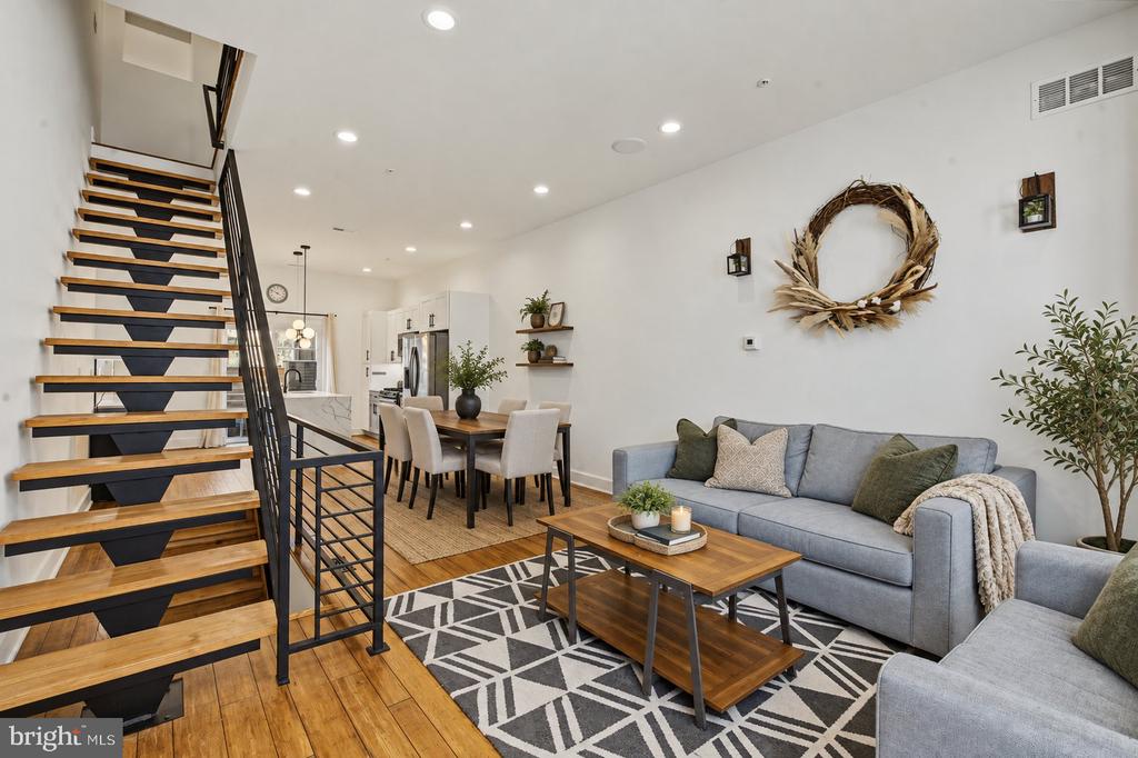 Open-plan living room with gray sofa, hardwood floors, and a striking open-riser staircase.