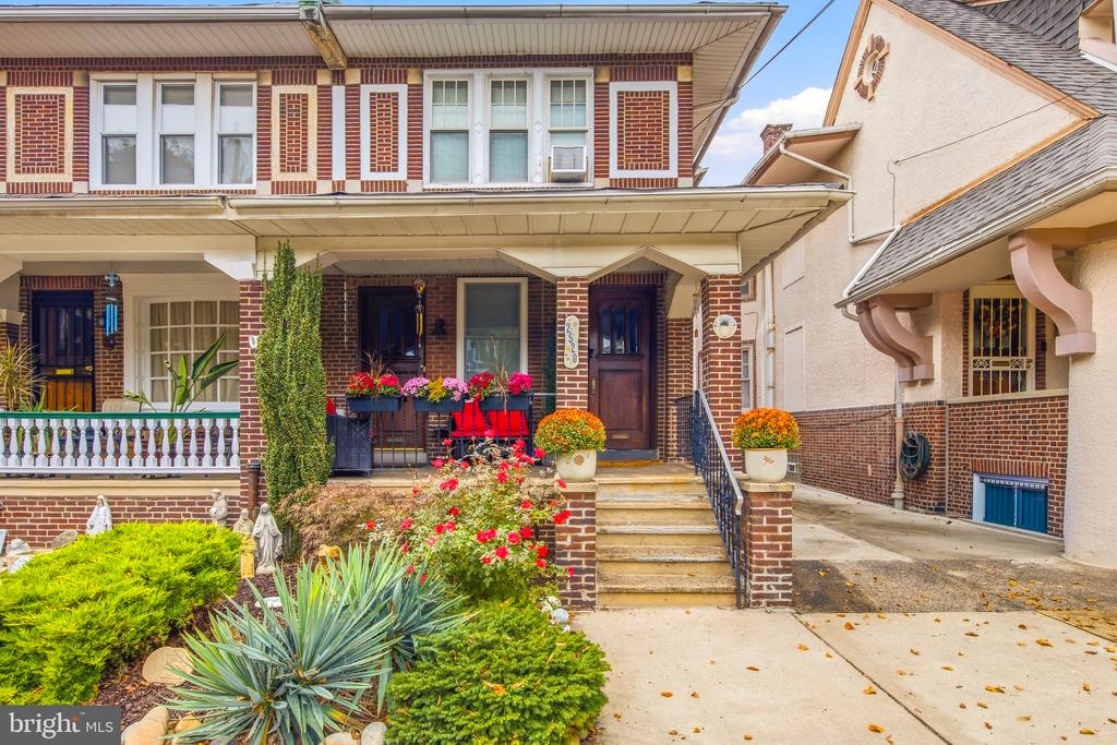 Red-brick rowhouse with a covered porch, central steps, and a colorful landscaped front garden.