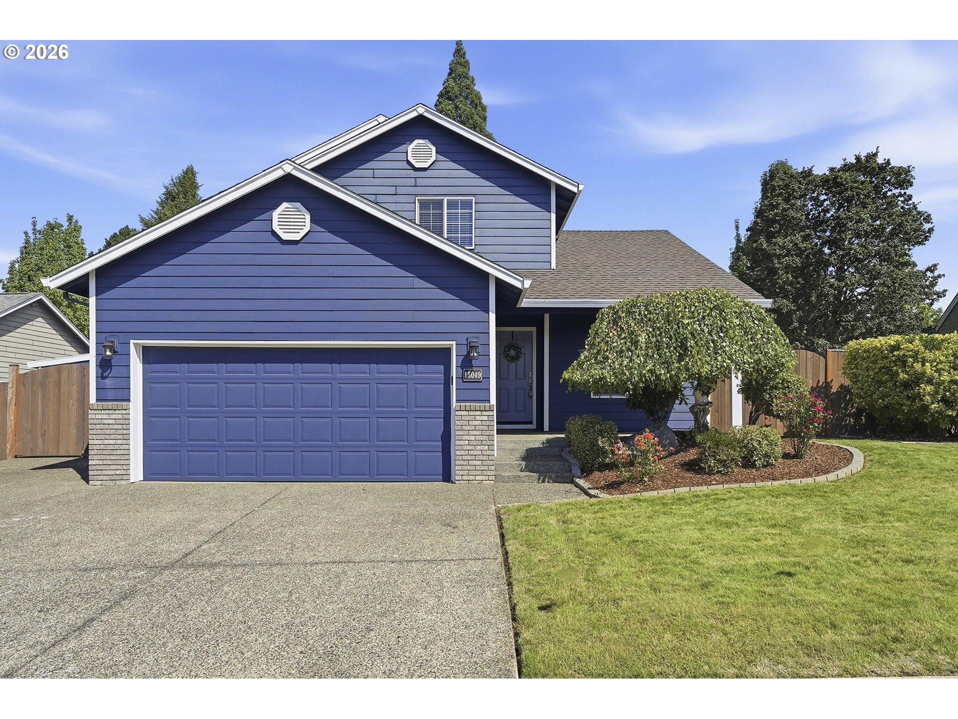 Blue two-story house with a white-trimmed garage, landscaped garden, and front lawn.
