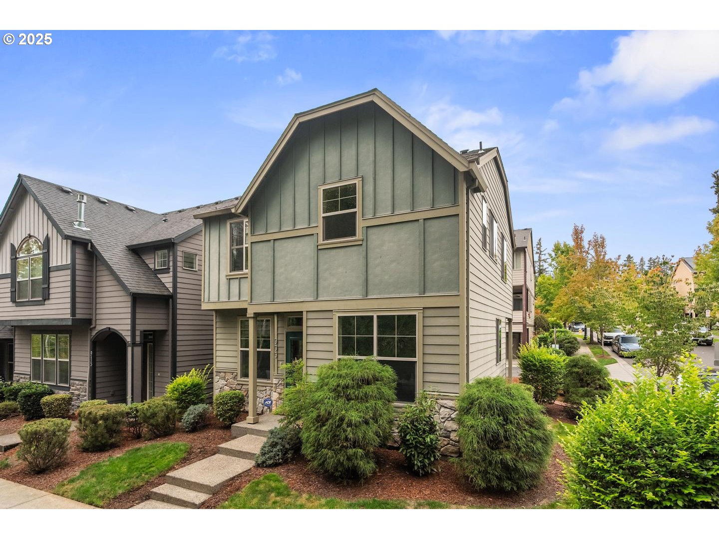 Gray-green townhouse with stone accents, landscaped shrubs, and a short walkway to the entrance.
