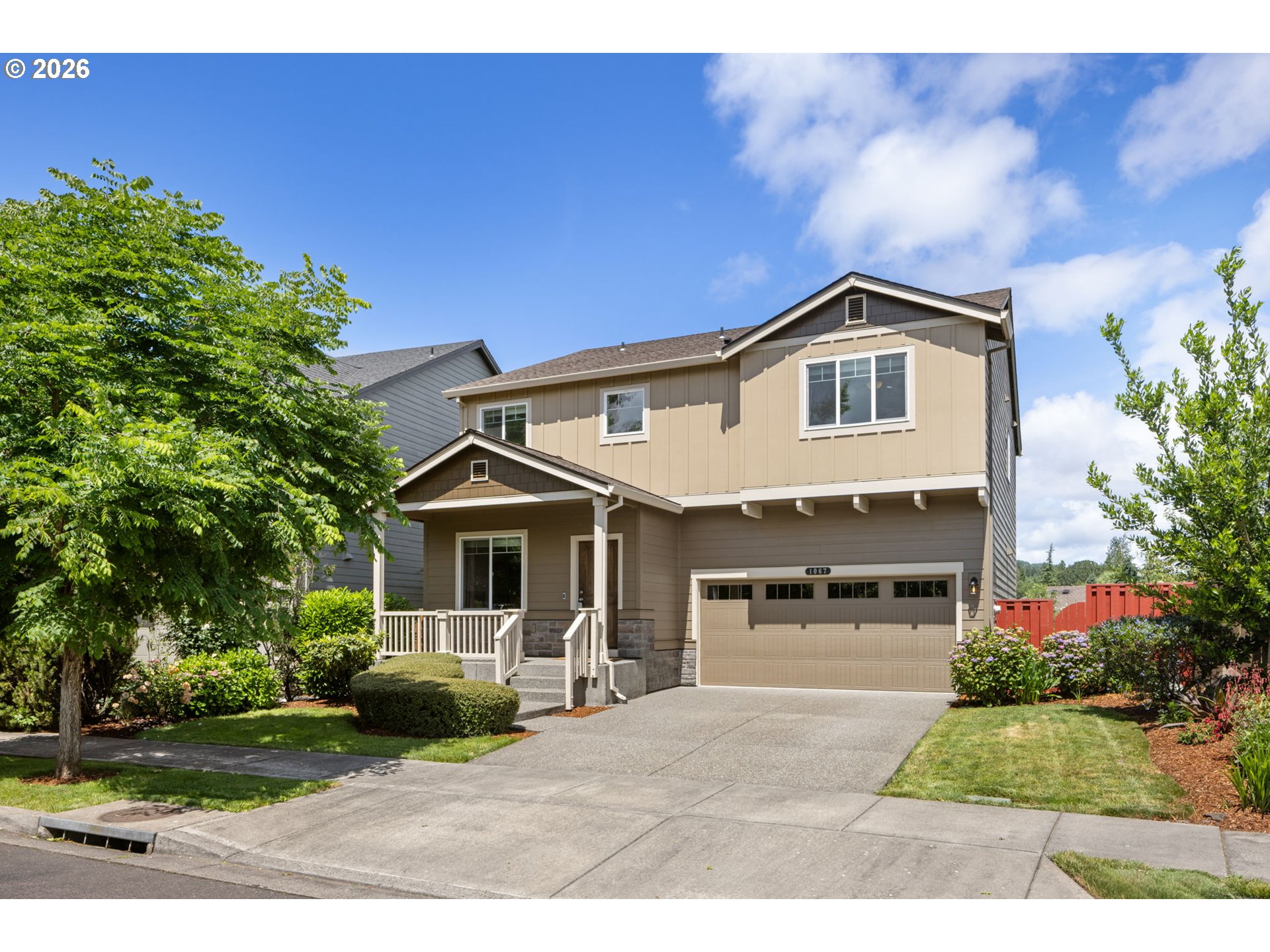 Two-story tan home with a covered porch, double garage, and landscaped front yard.