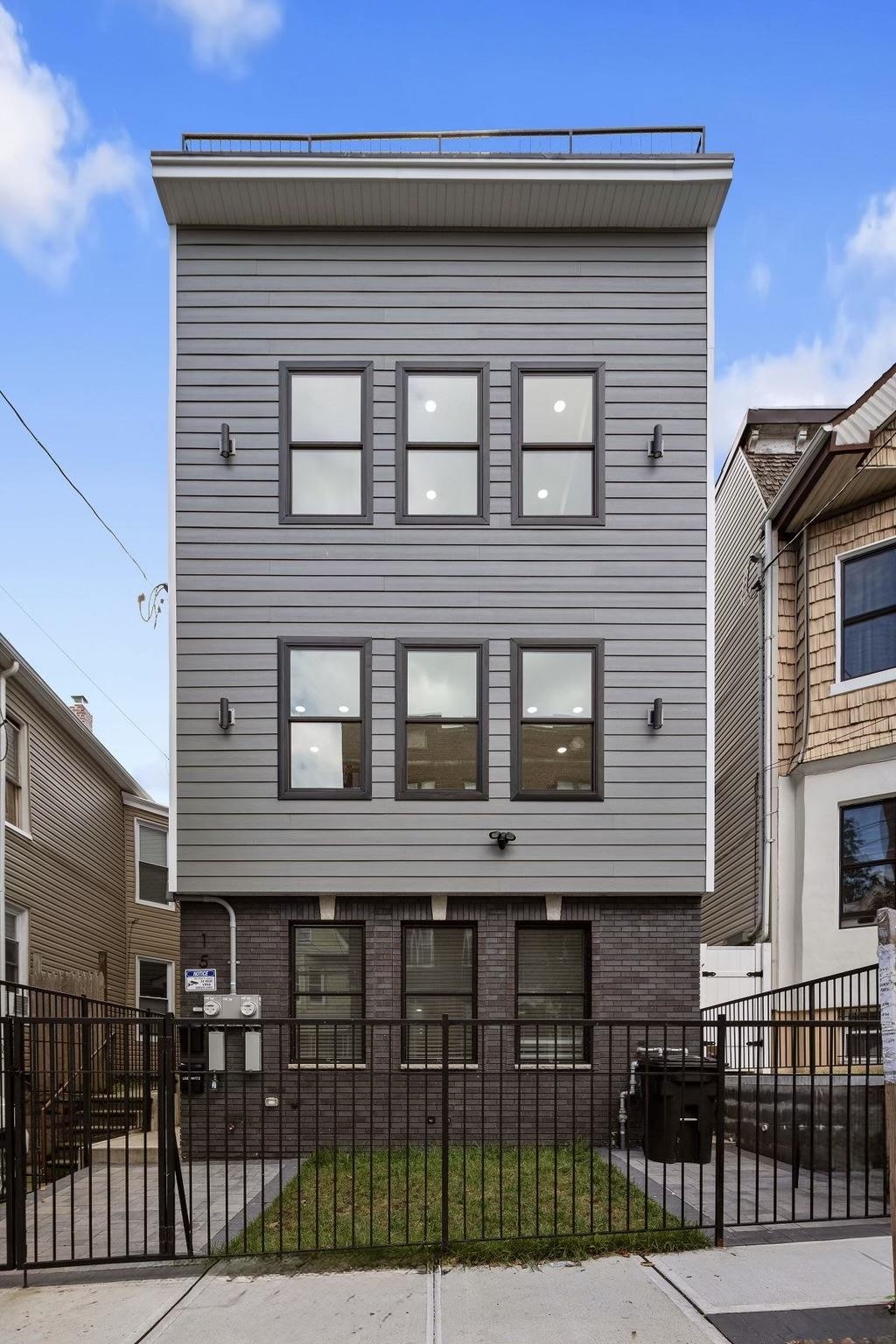 Modern gray multi-story home with a fenced front yard and rooftop railing.
