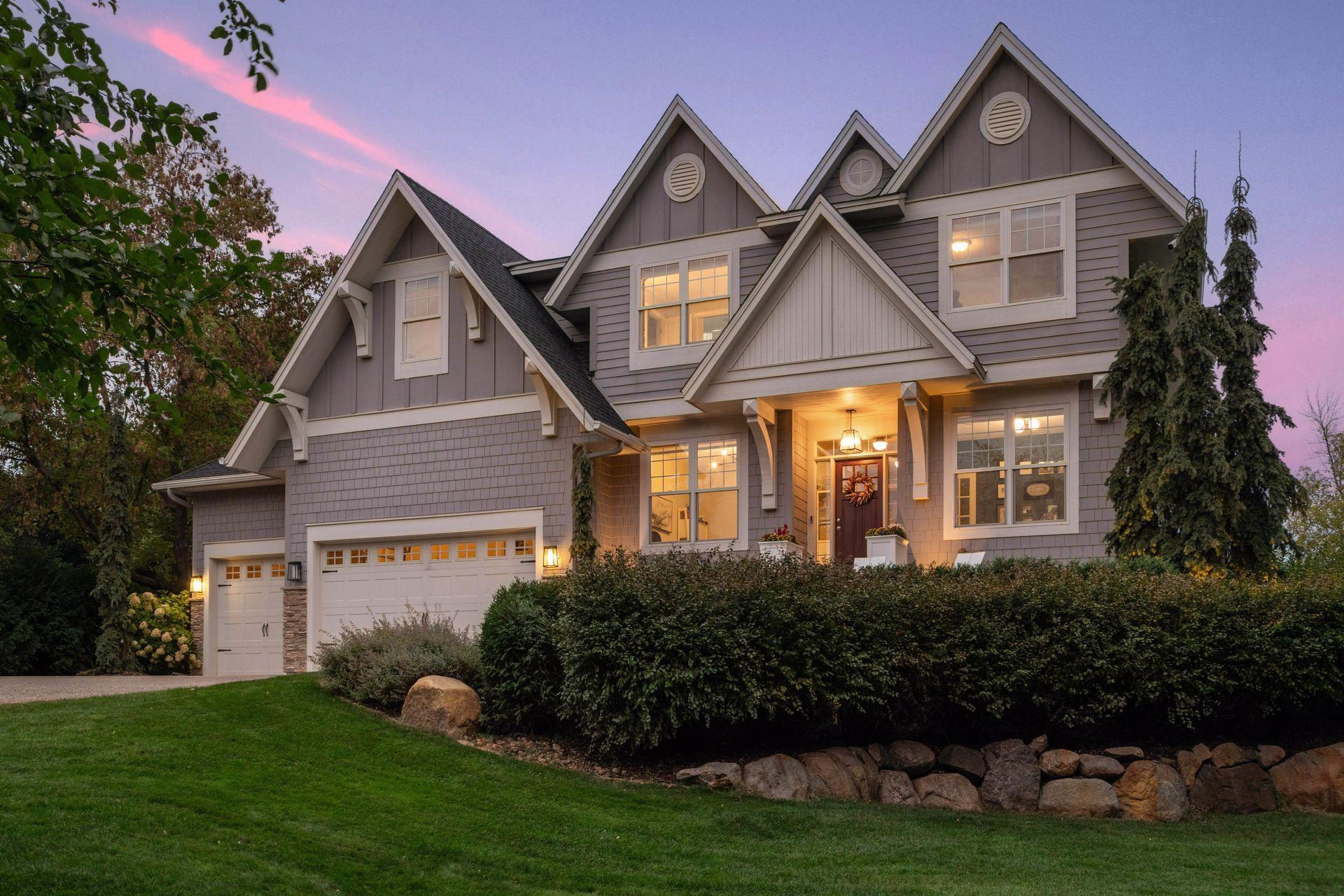 Gray multi-gabled house with a double garage and warmly lit entrance at dusk.