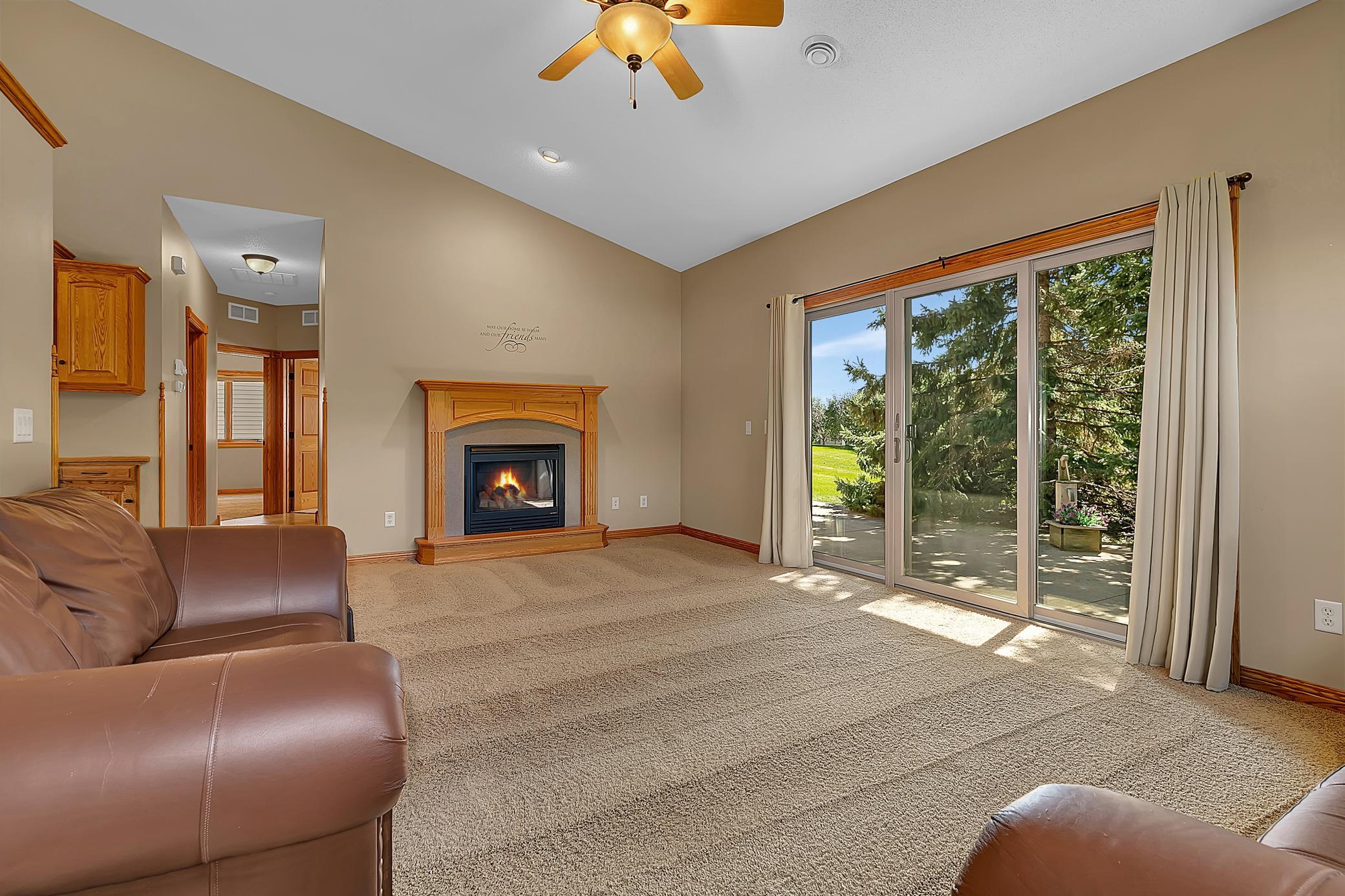 Living room with a lit wood-mantel fireplace, leather seating, and sliding doors to a sunny patio.
