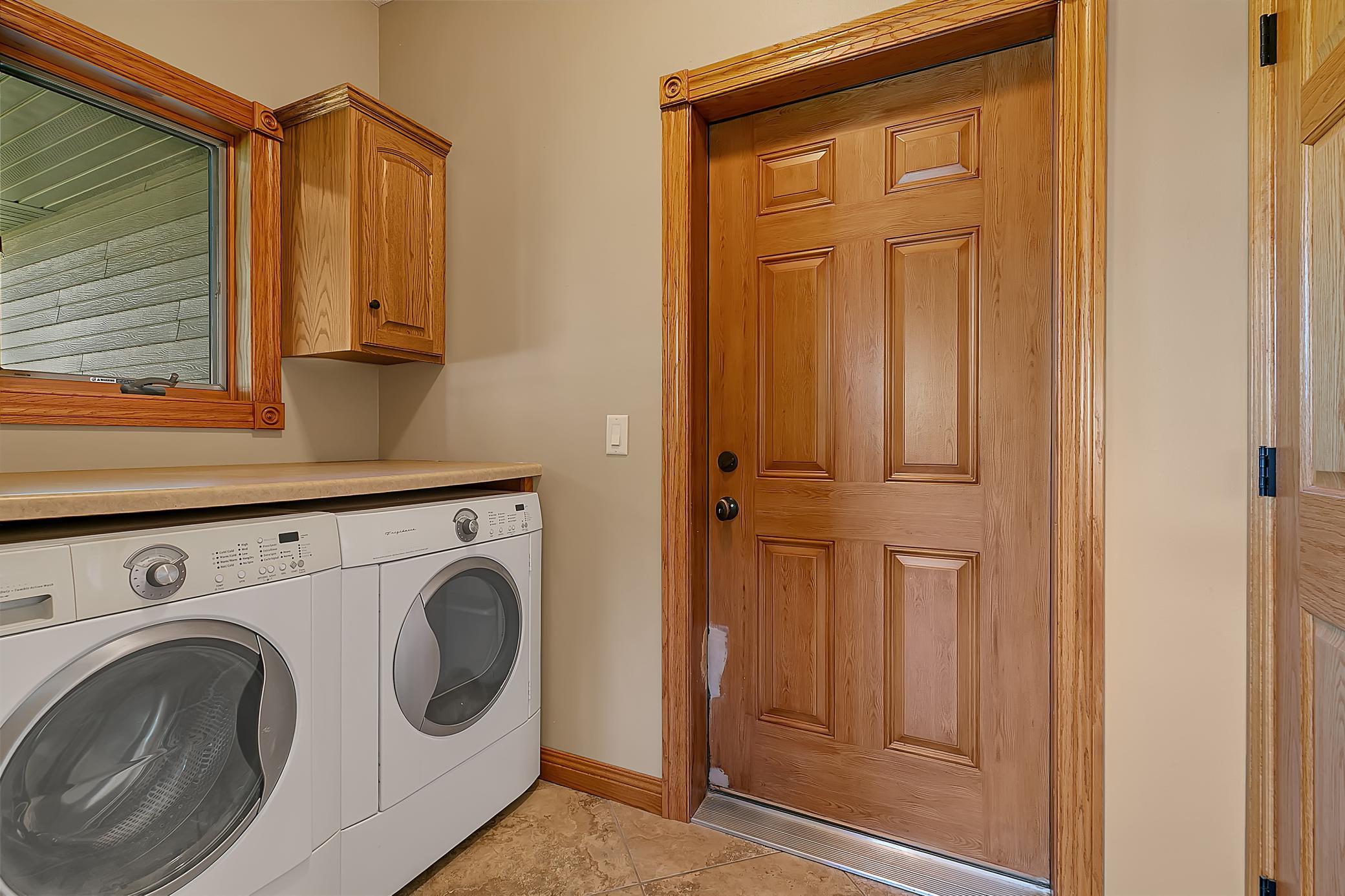Laundry and entry area with front-loading washer and dryer beside a paneled wood door.