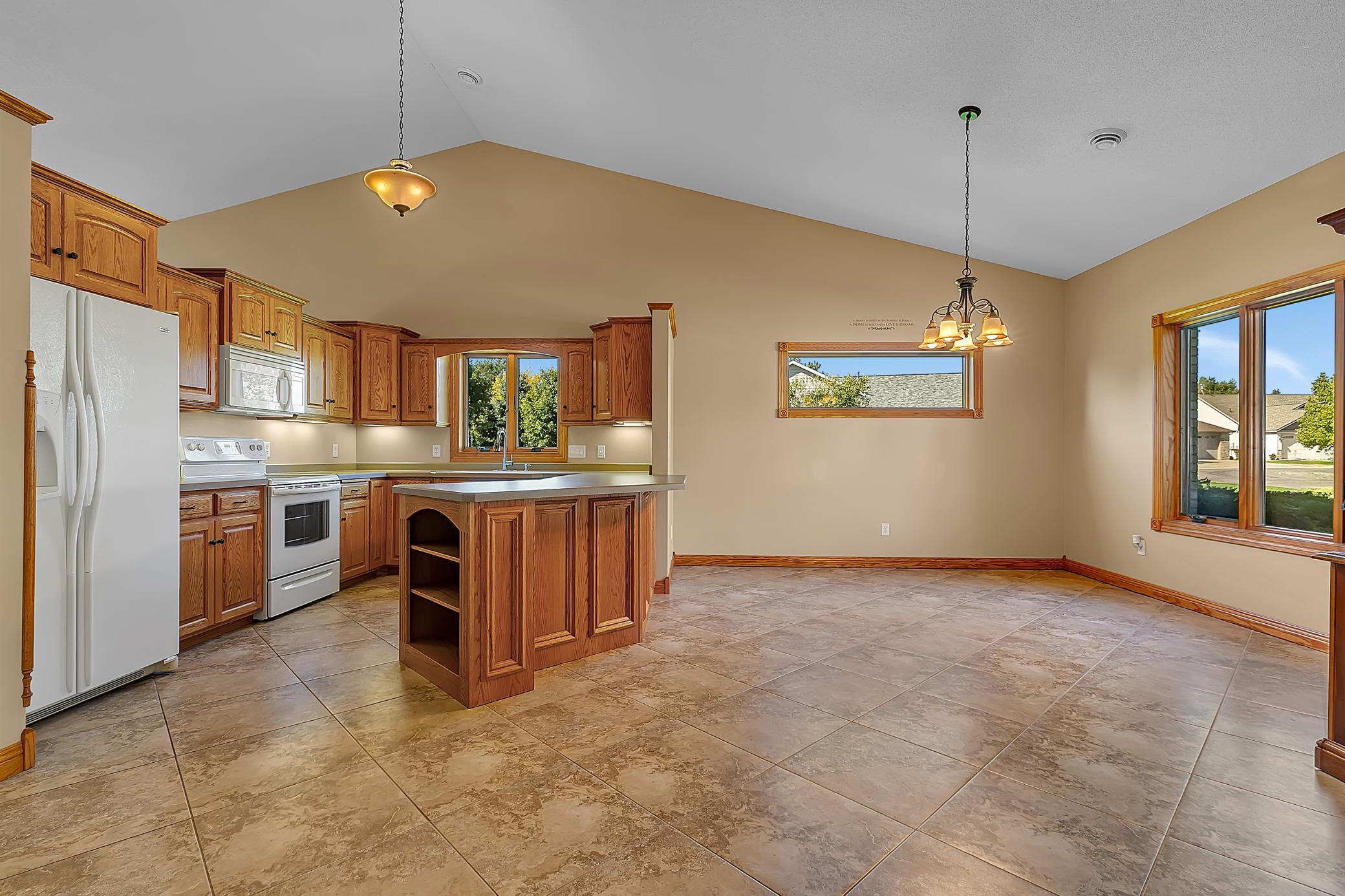 Open kitchen with wood cabinetry, a central island, white appliances, and tile flooring.