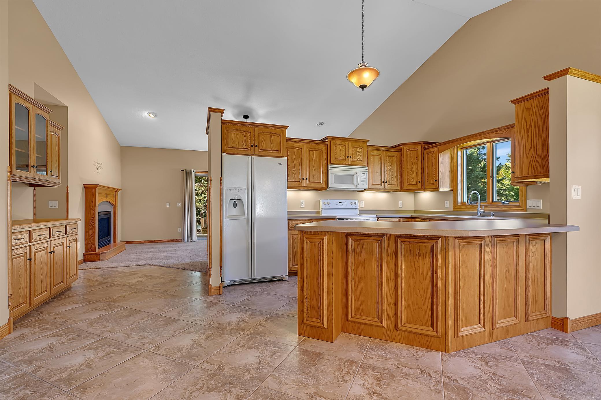 Kitchen with extensive wood cabinetry, a large island, tiled floors, and a fireplace in the adjoining room.