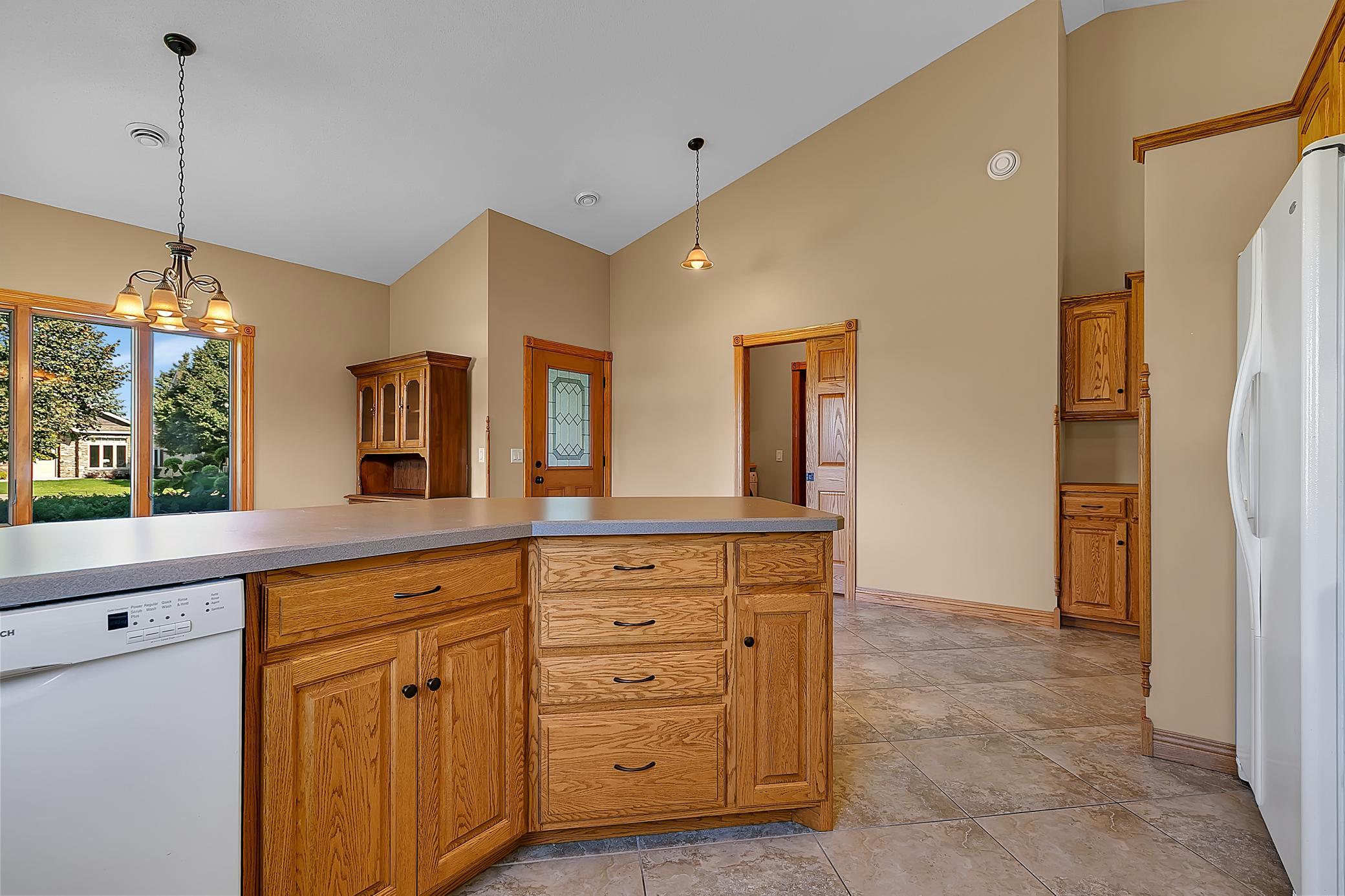 Kitchen with a large wood-cabinet island, tile floor, and wide window overlooking greenery.
