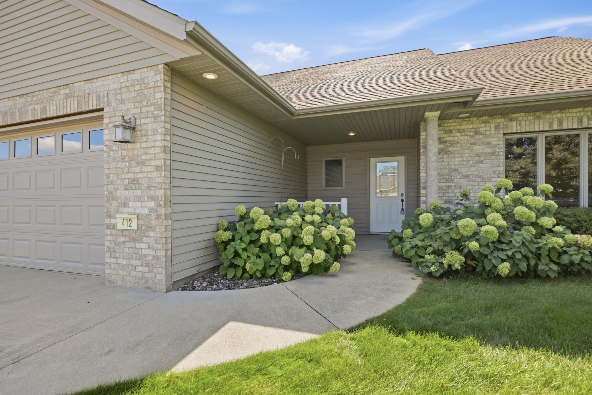 Home exterior with a covered entry, double garage, and flowering hydrangeas beside the walkway.