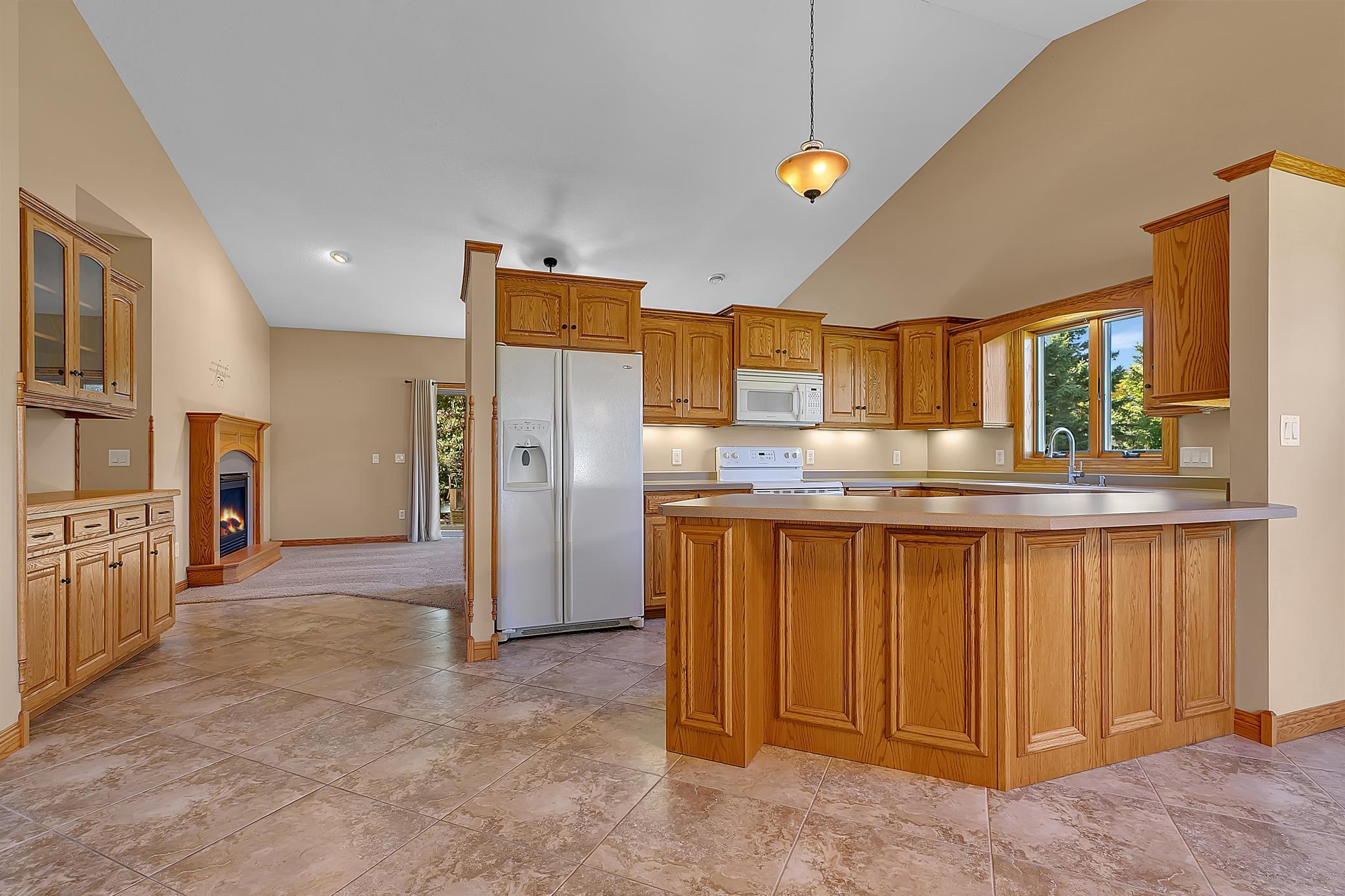 Kitchen with honey-toned wood cabinets, a large peninsula island, and a fireplace in the adjoining living area.