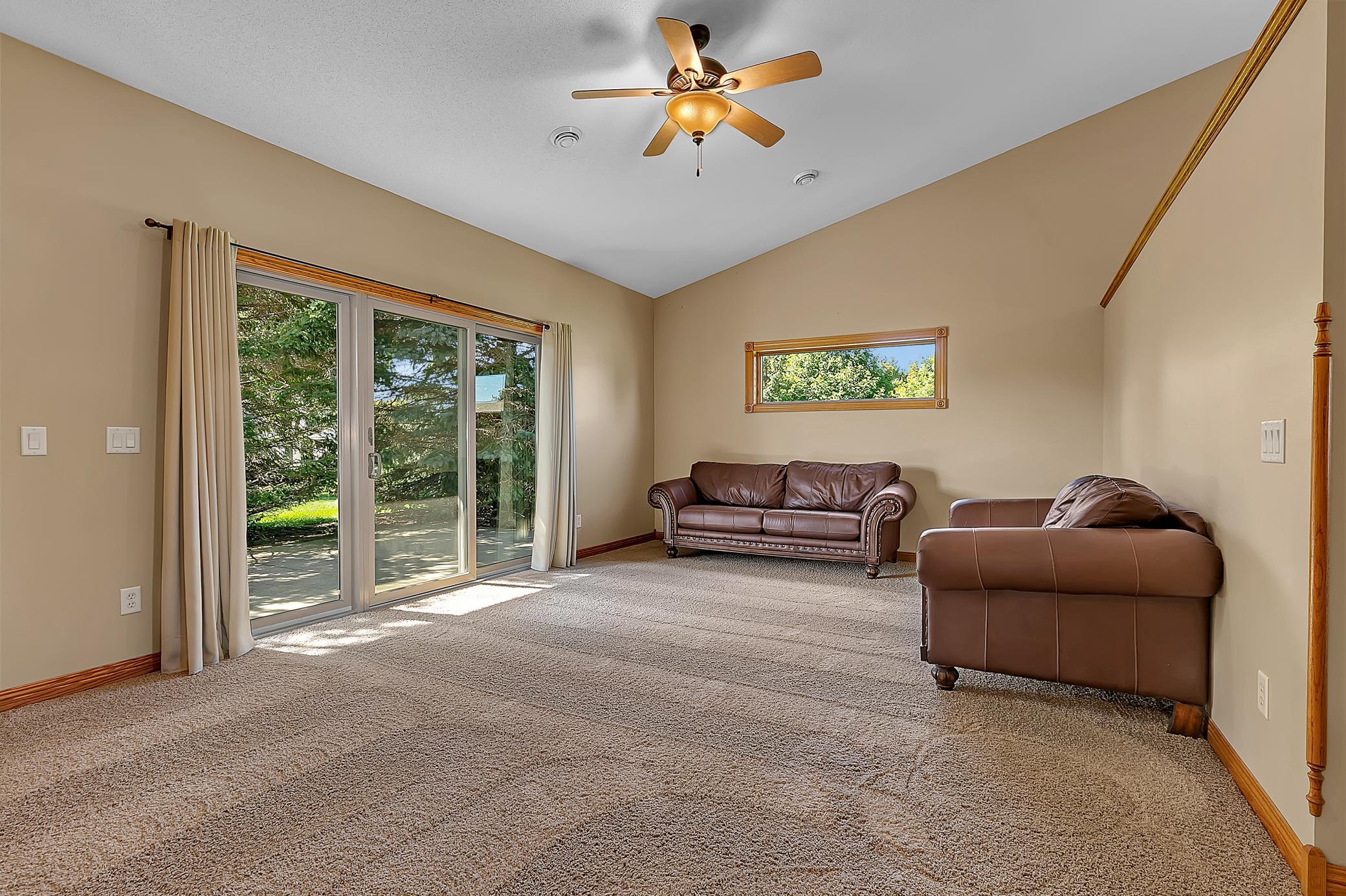 Living room with brown leather sofas, carpet, and sliding glass doors overlooking trees.