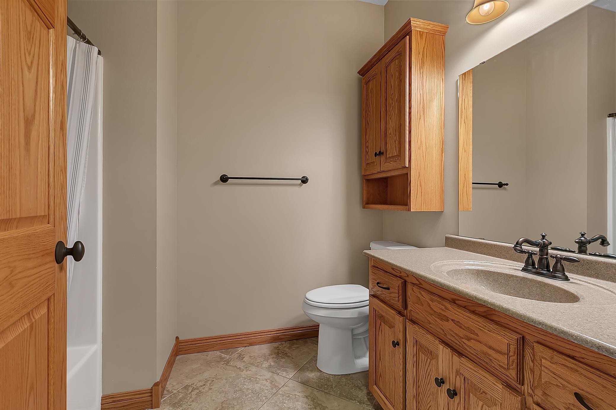 Bathroom with oak vanity and wall cabinet, large mirror, toilet, and curtained tub-shower.