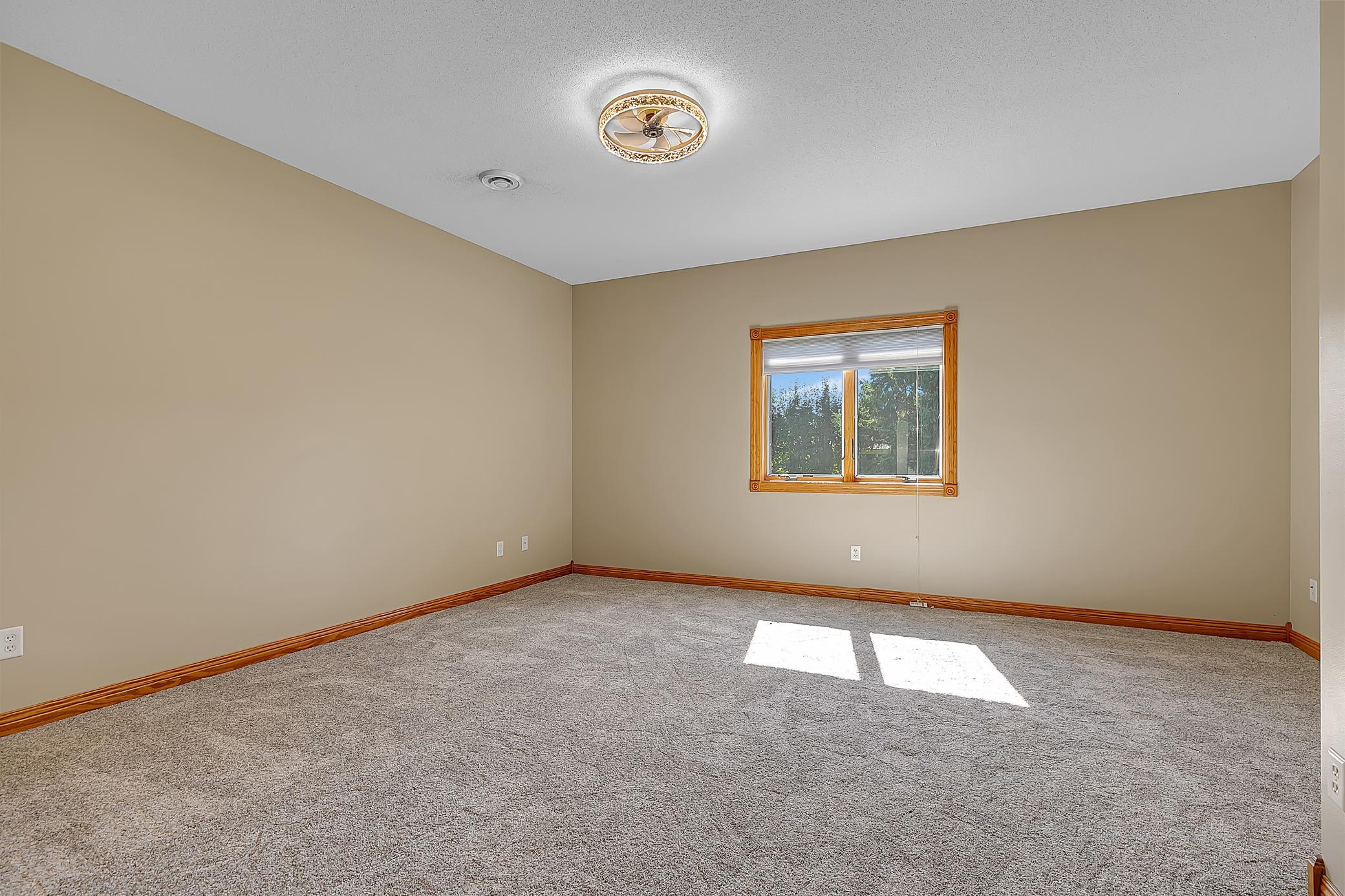 Empty carpeted room with beige walls, wood trim, and a window.
