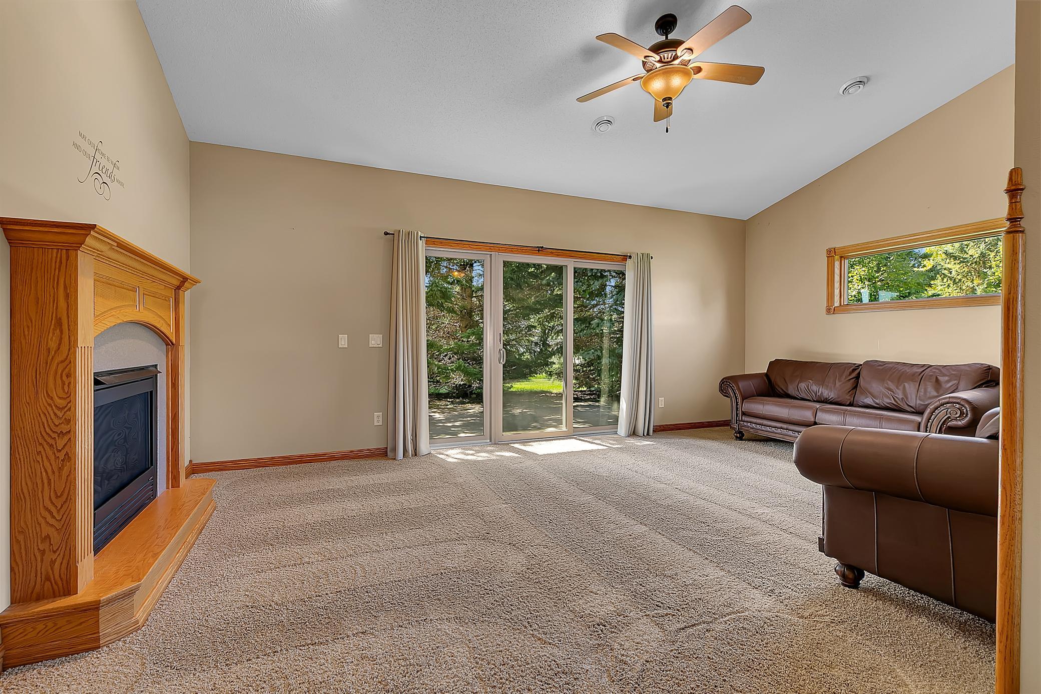 Living room with a wood-trimmed fireplace, brown leather sofas, and sliding glass doors to a leafy yard.