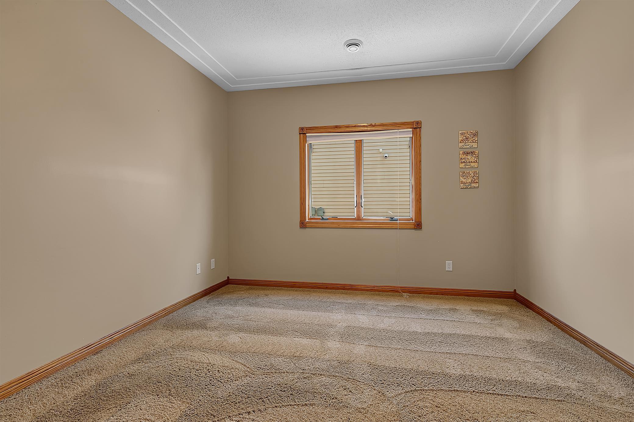 Empty carpeted room with a wood-trimmed window, closed blinds, and beige walls.