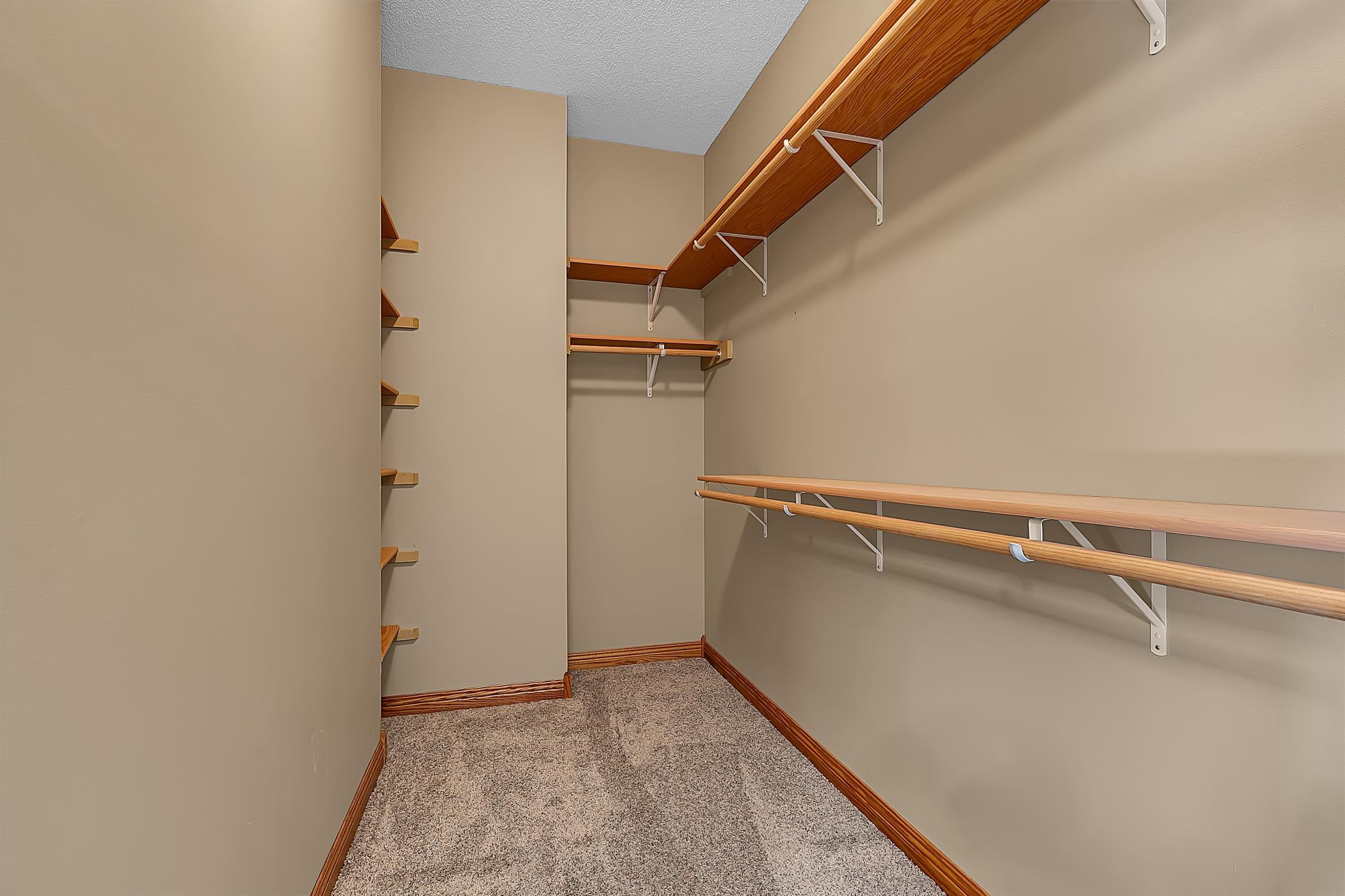 Walk-in closet with wood shelving and hanging rods along beige walls.