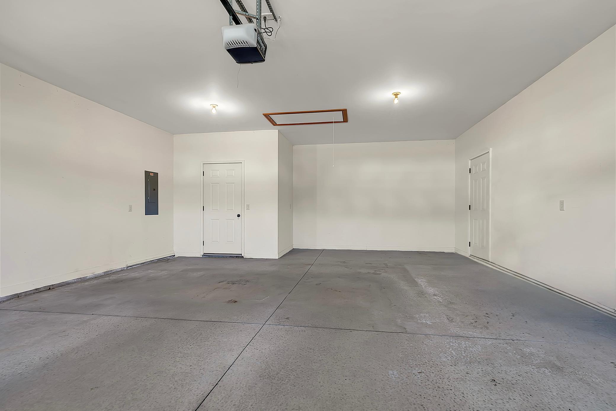 Empty garage with a concrete floor, two white doors, and an overhead garage door opener.