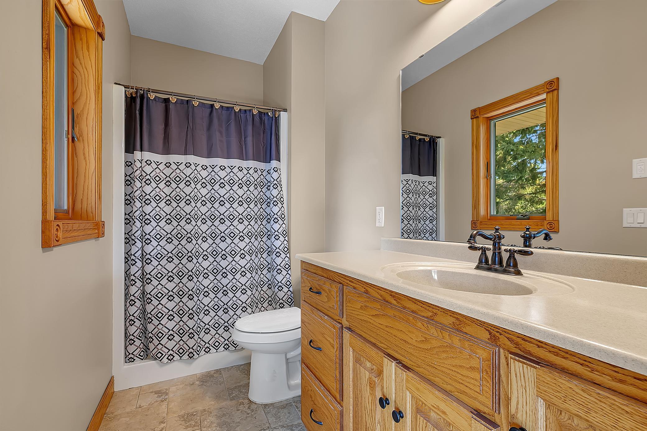 Bathroom with a honey-toned wood vanity, wood-trimmed window, and geometric shower curtain.