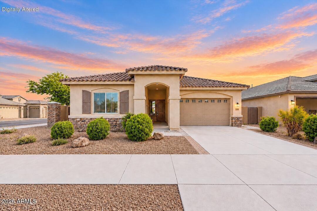 Single-story stucco home with stone accents, desert landscaping, and a sunset sky.