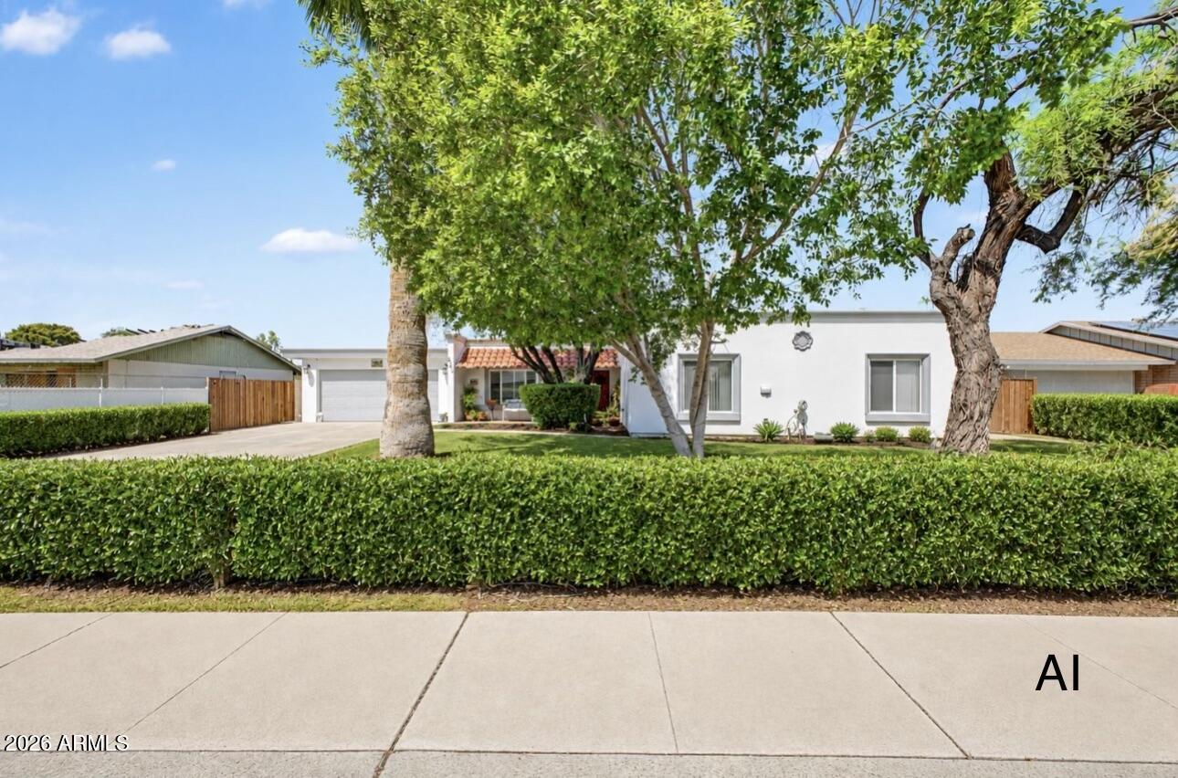 Single-story white home behind a trimmed hedge, with mature trees and a tiled entry.