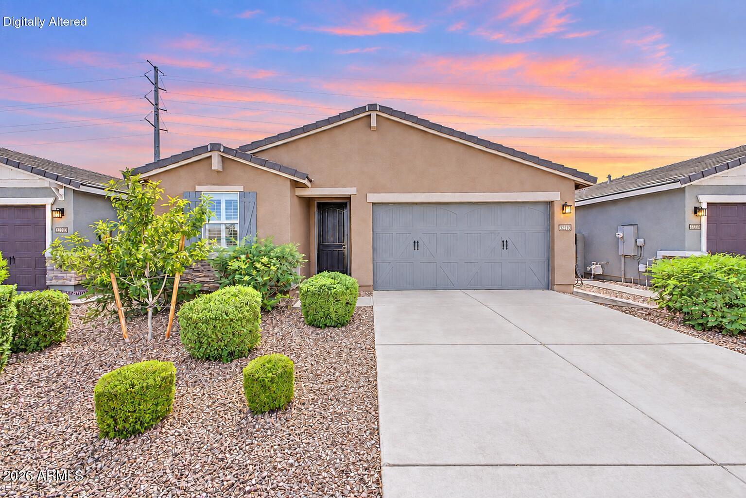 Single-story stucco home with a double garage, broad driveway, and desert landscaping beneath a pink sunset sky.